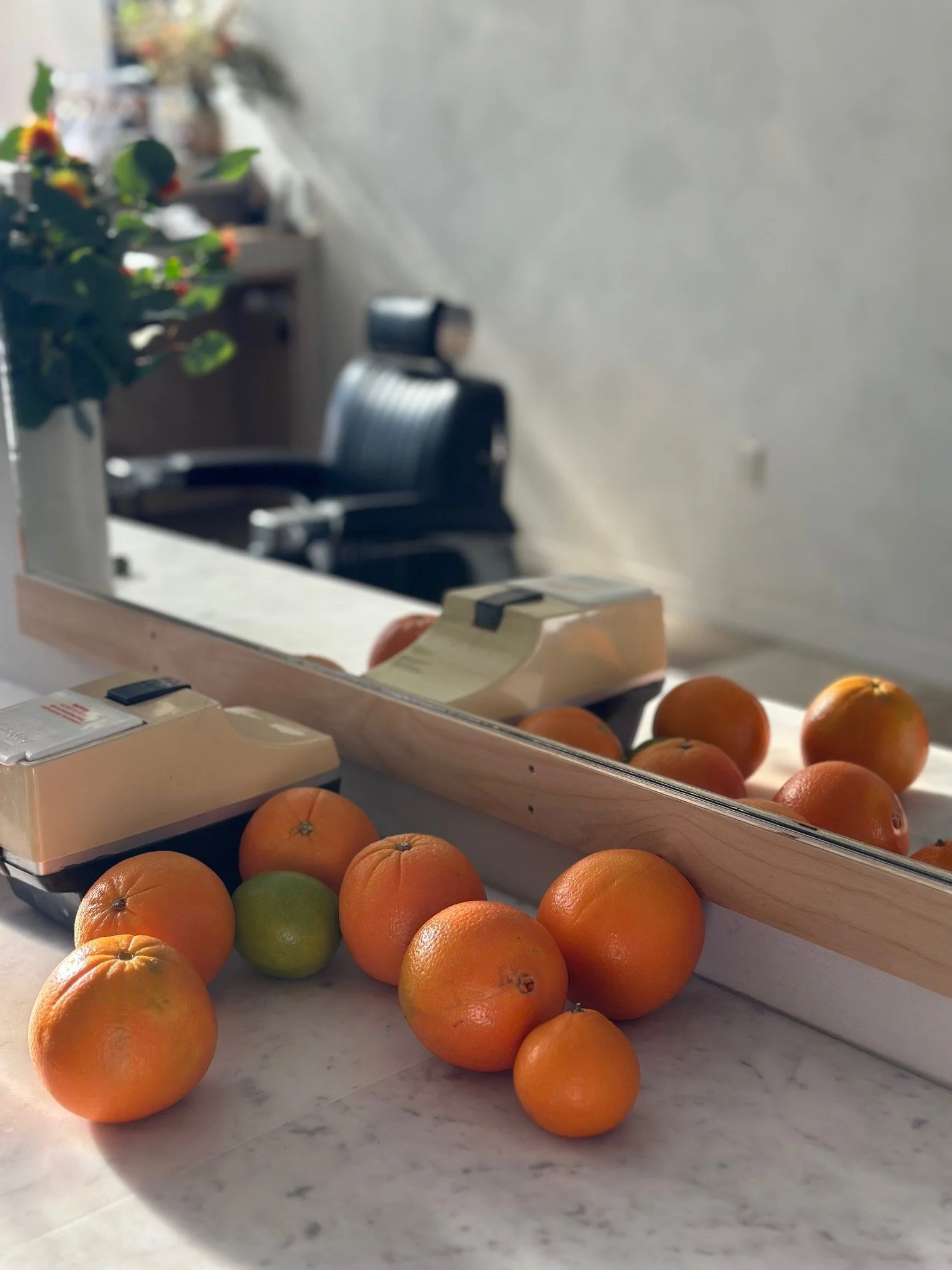Oranges and a lime on a marble countertop, with a mirror and a black office chair reflected in the background to reflect wellness services offered in the barbershop.