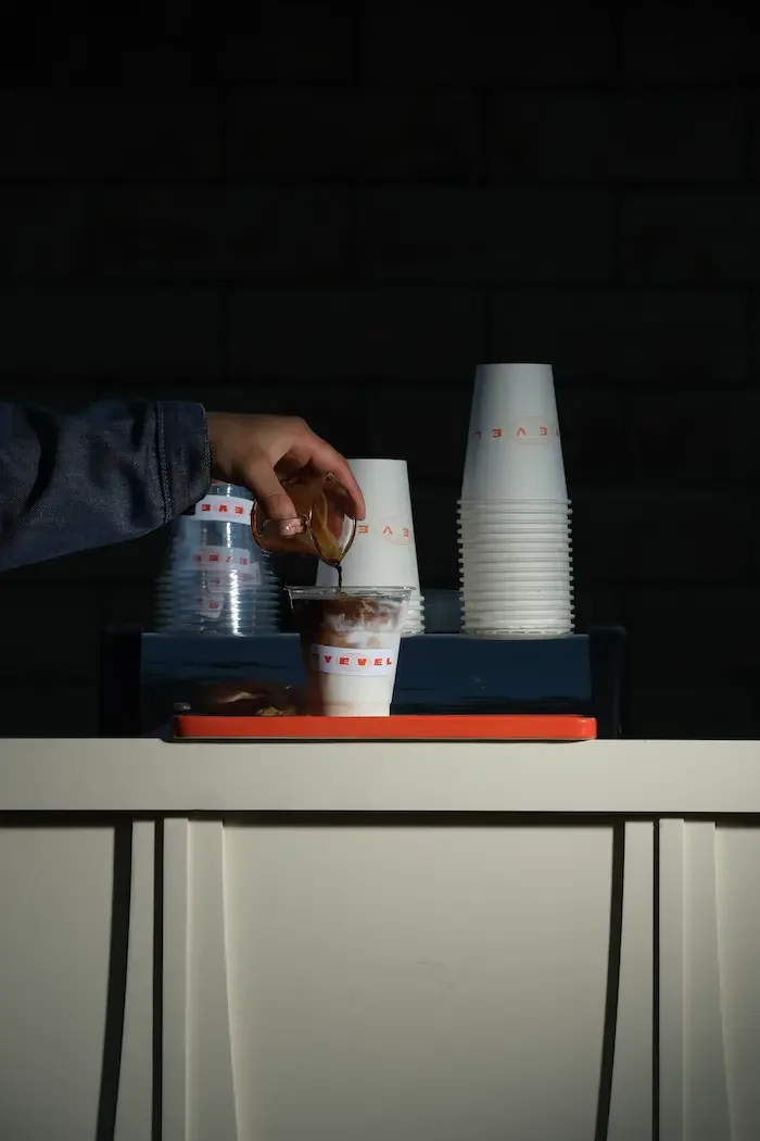 person pouring espresso into a cup of milk with cup that says eyevel