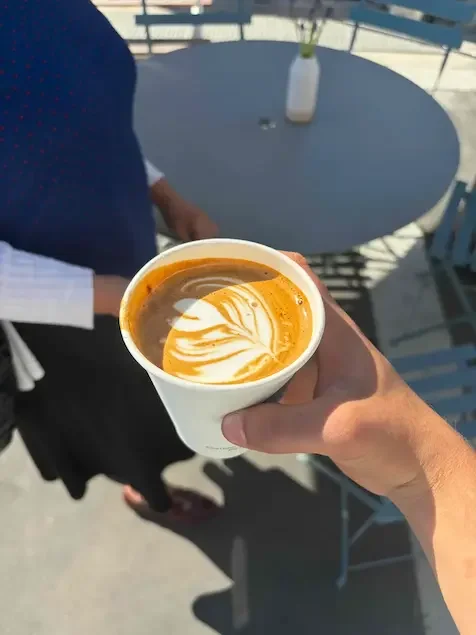 person holding latte with latte art that resembles a rosetta handing to customer
