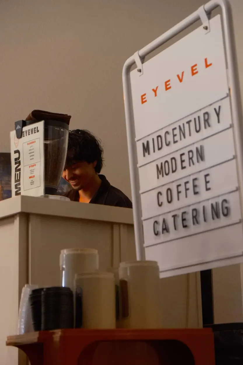 Man smiles with sign saying midcentury modern coffee cateing.