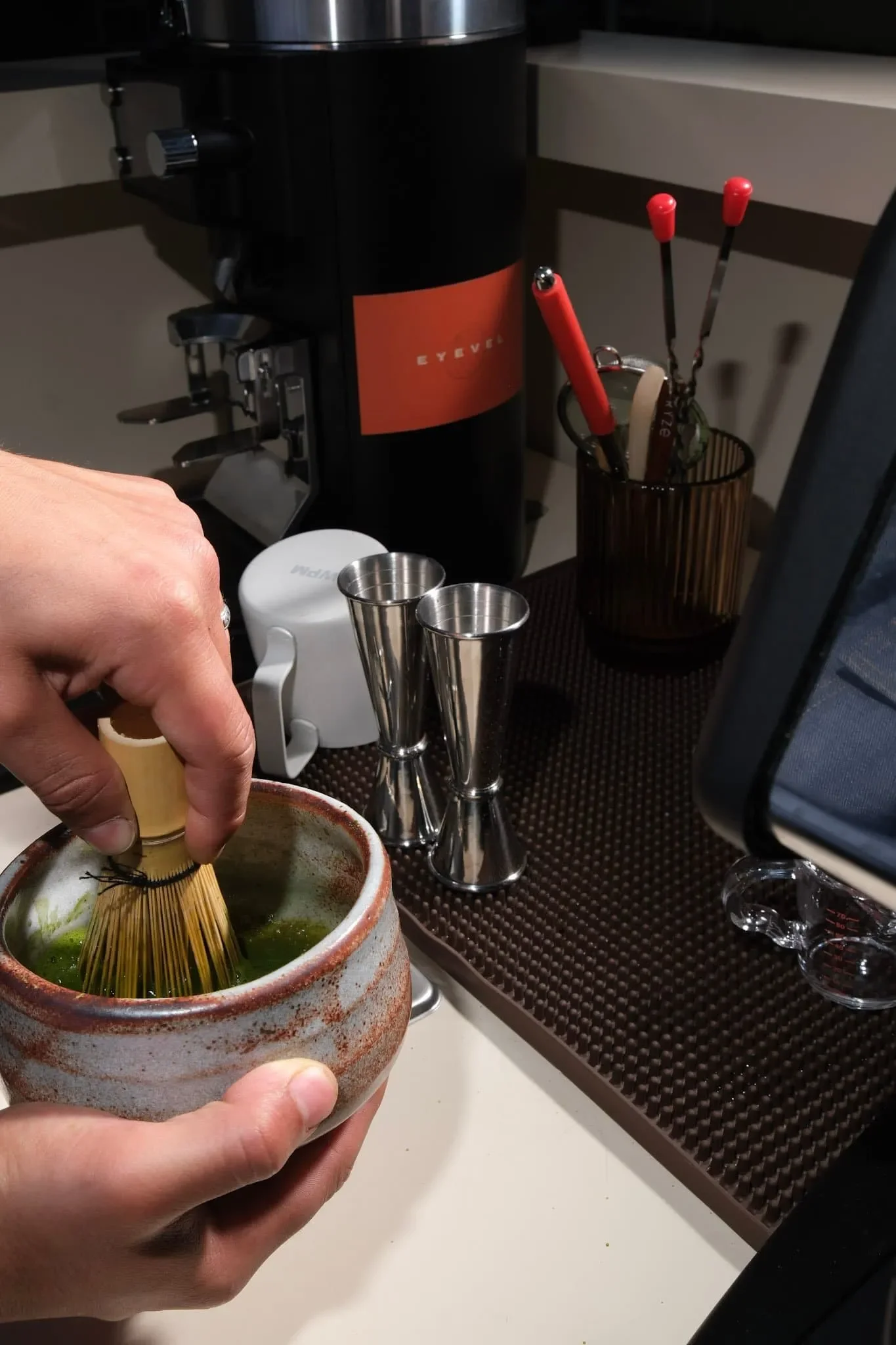 Person using a bamboo whisk to prepare matcha tea in a ceramic bowl.