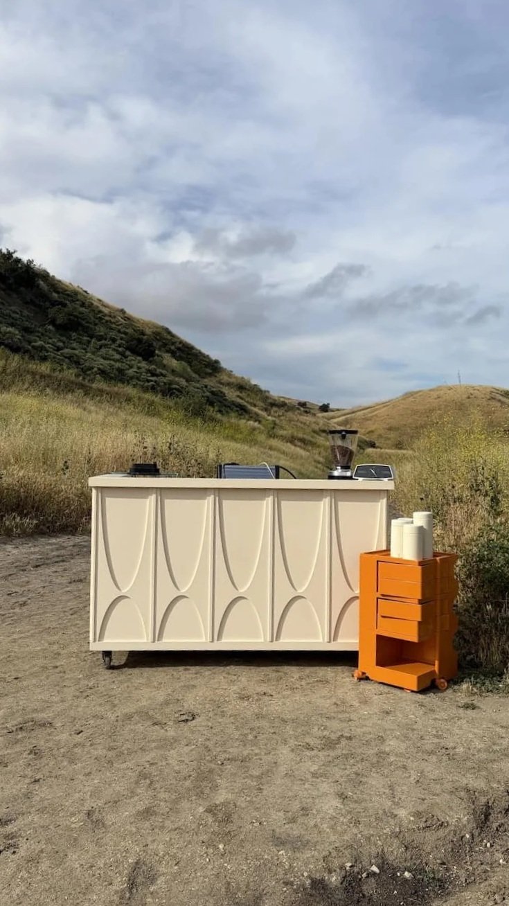 Mobile espresso catering at an event outdoors on a dirt path and grassy hills.