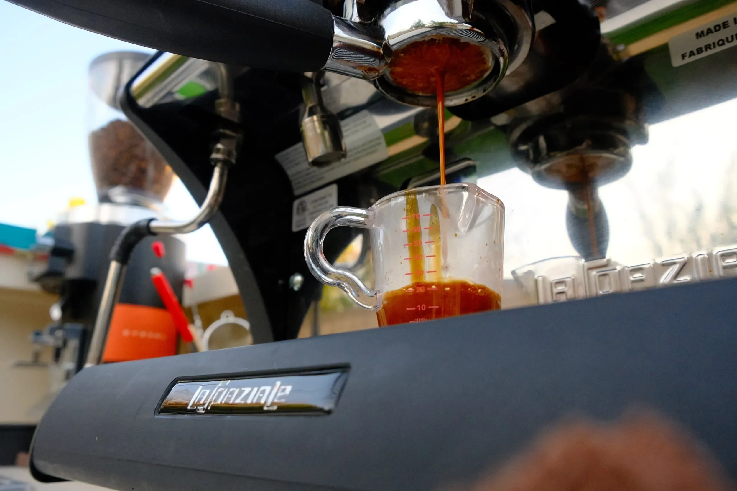 Coffee brewing under a coffee machine with a clear measuring cup below catching the coffee.