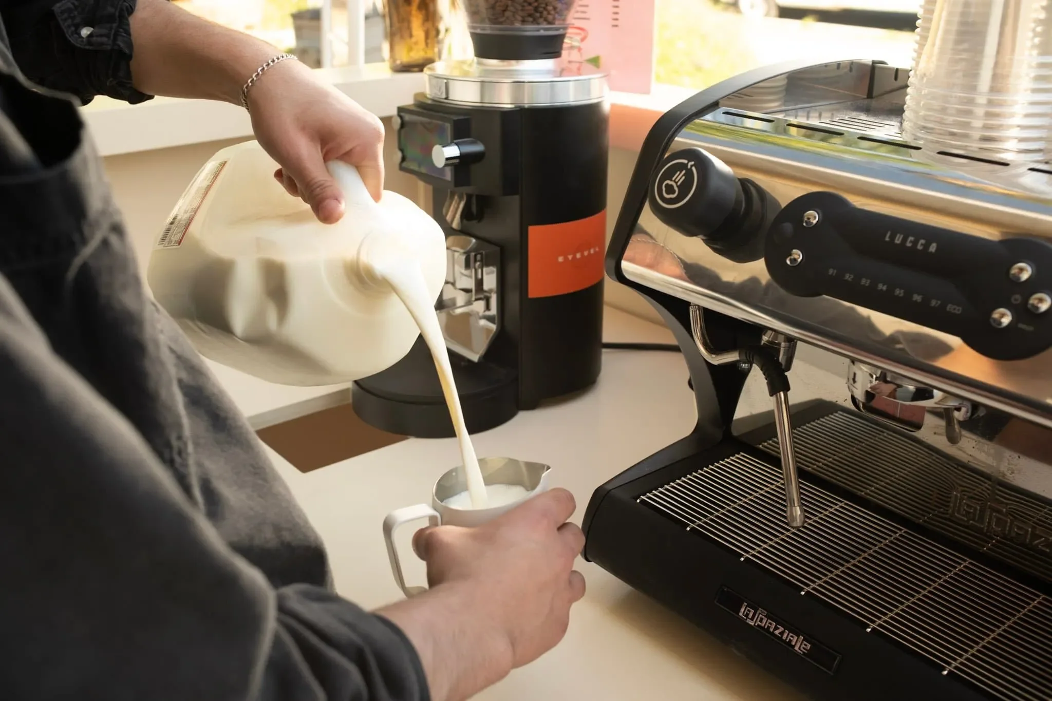 A person pouring milk into a coffee machine to make a latte.