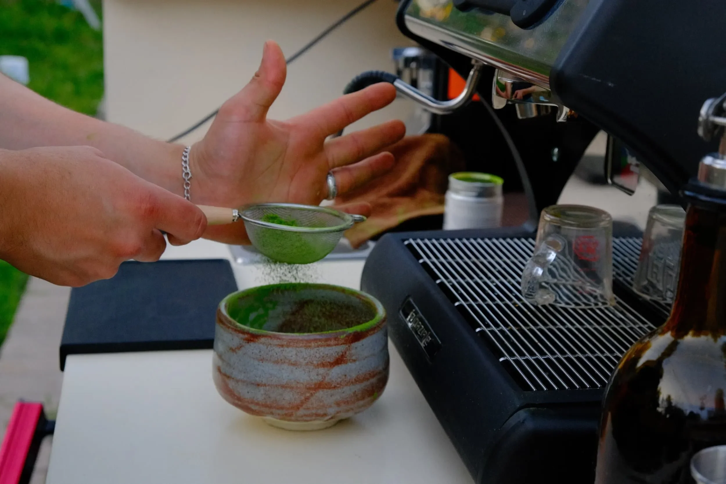 Person using a coffee filter to sprinkle matcha into a cup near a coffee machine.