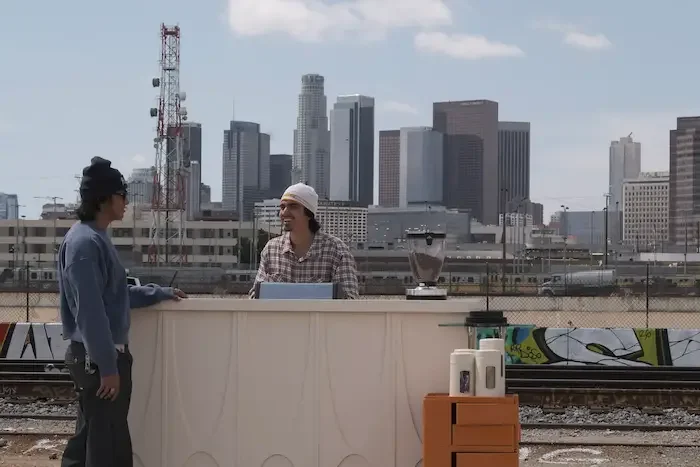 A customer stand at a coffee cart ordering with a mobile barista standing behind the coffee cart , serving mobilecoffee catering against Los Angeles skyline.