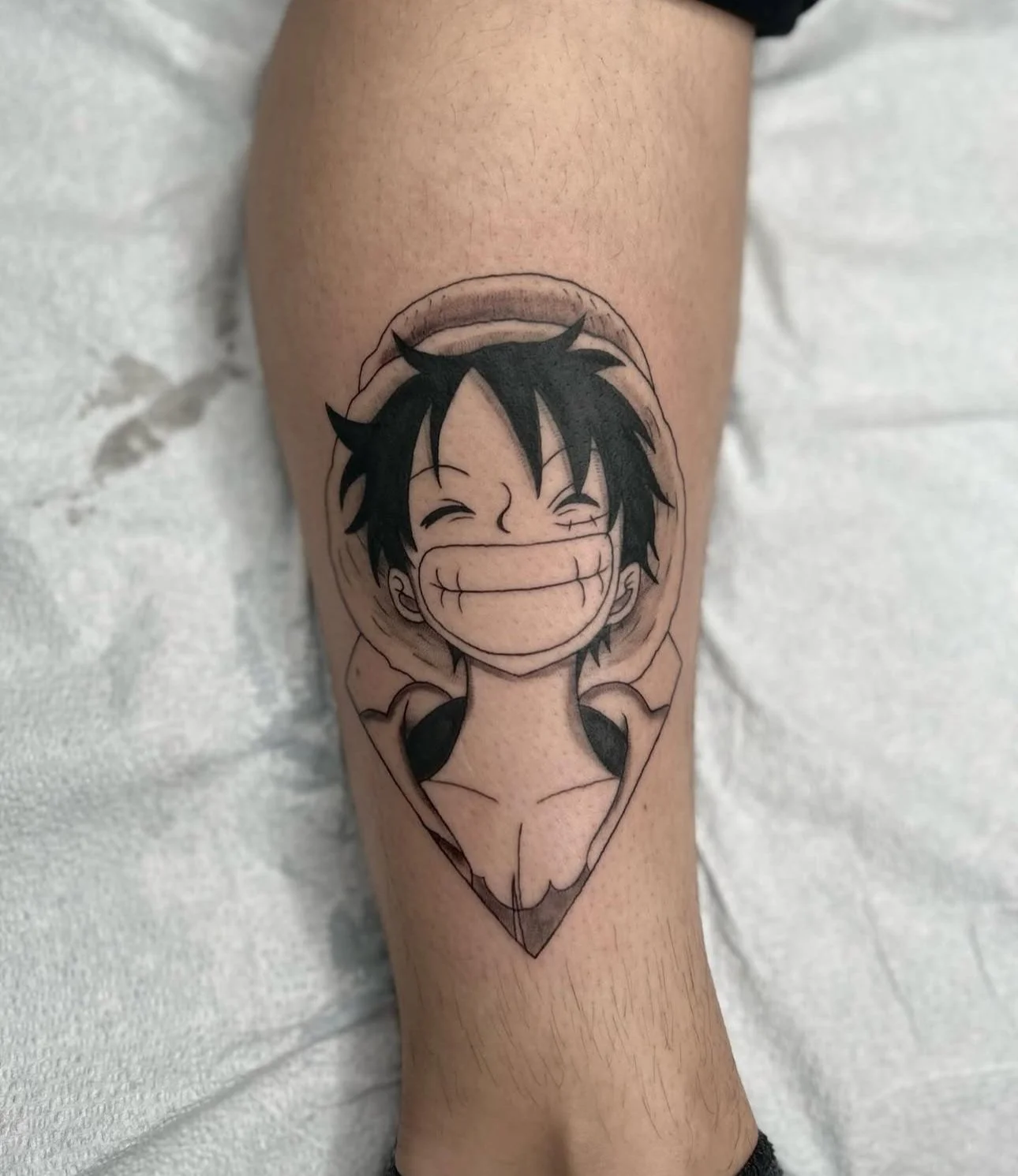 Black and gray tattoo of a smiling anime boy with spiky hair inside a diamond shape on a person's forearm.