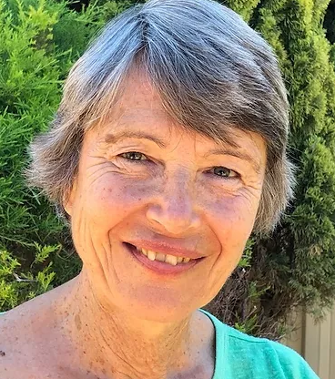 A smiling woman with short gray hair outdoors, with green foliage in the background.
