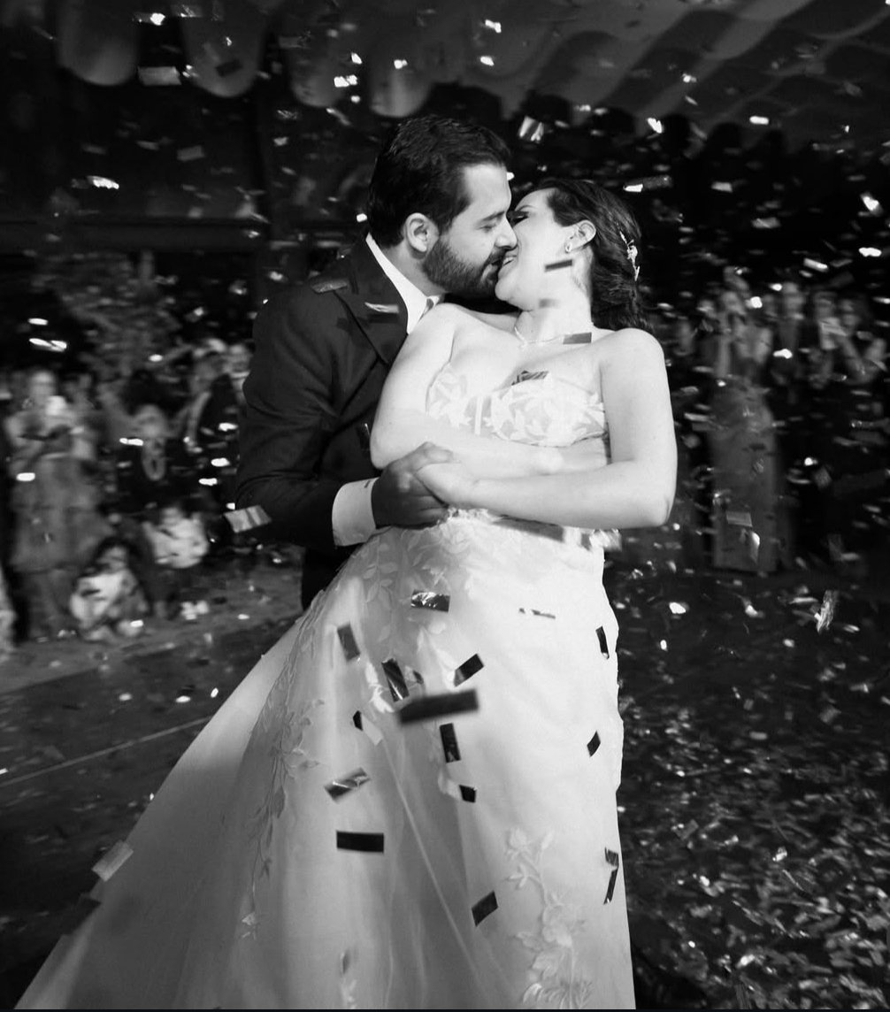Una pareja bailando y besándose en su boda, rodeados de confeti, en una celebración.