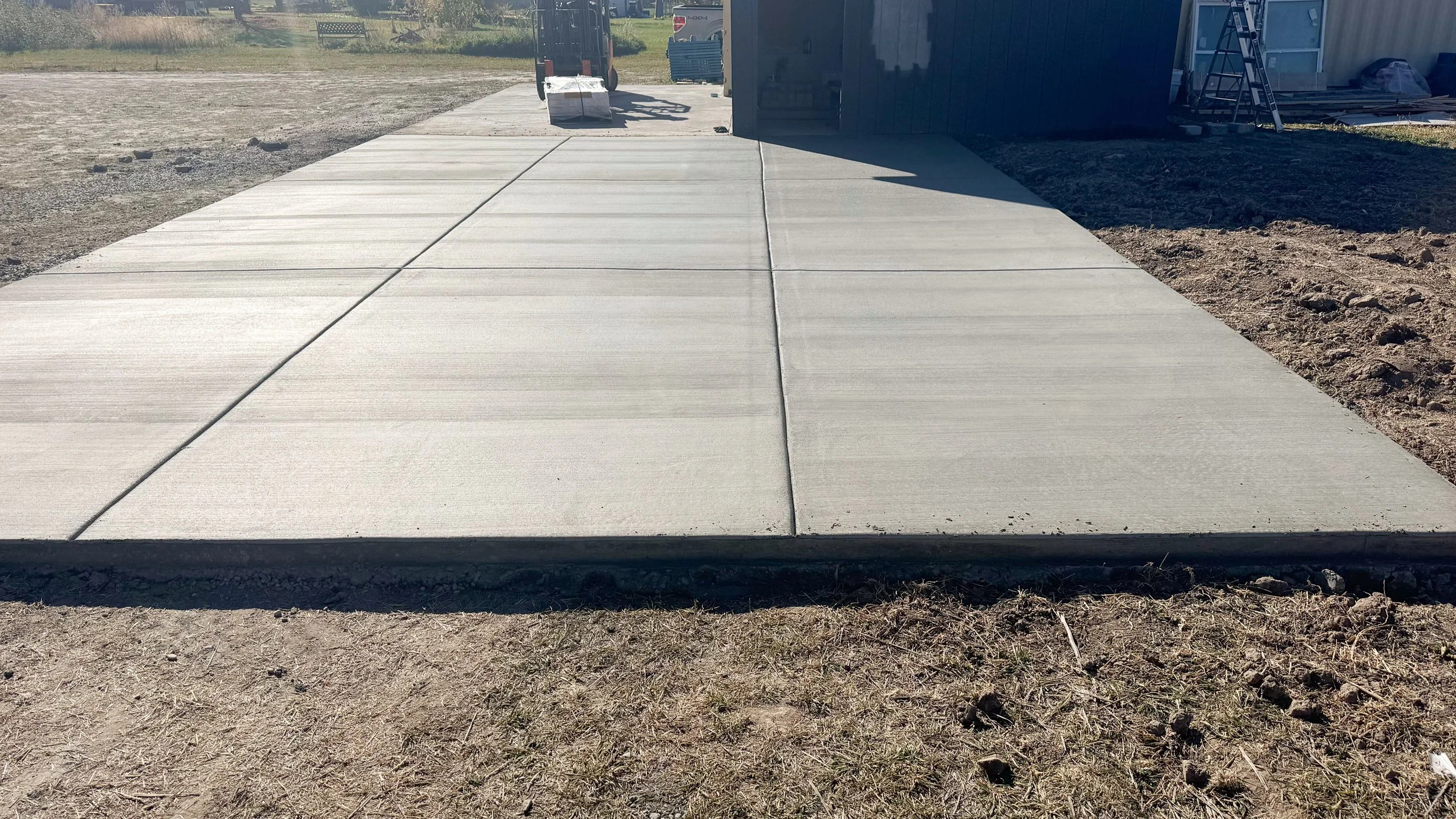 Newly poured concrete sidewalk leading to a building with construction tools and materials nearby, on a sunny day.