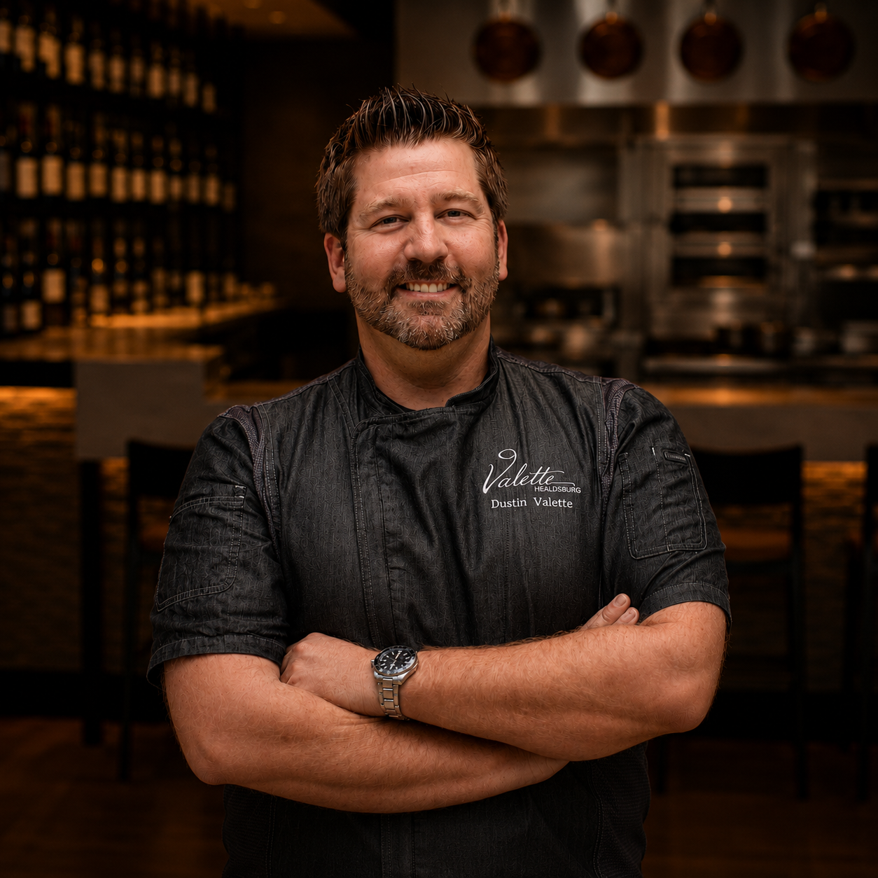 Portrait of Chef Dustin Valette in a chef coat with arms crossed smiling in a barn doorway
