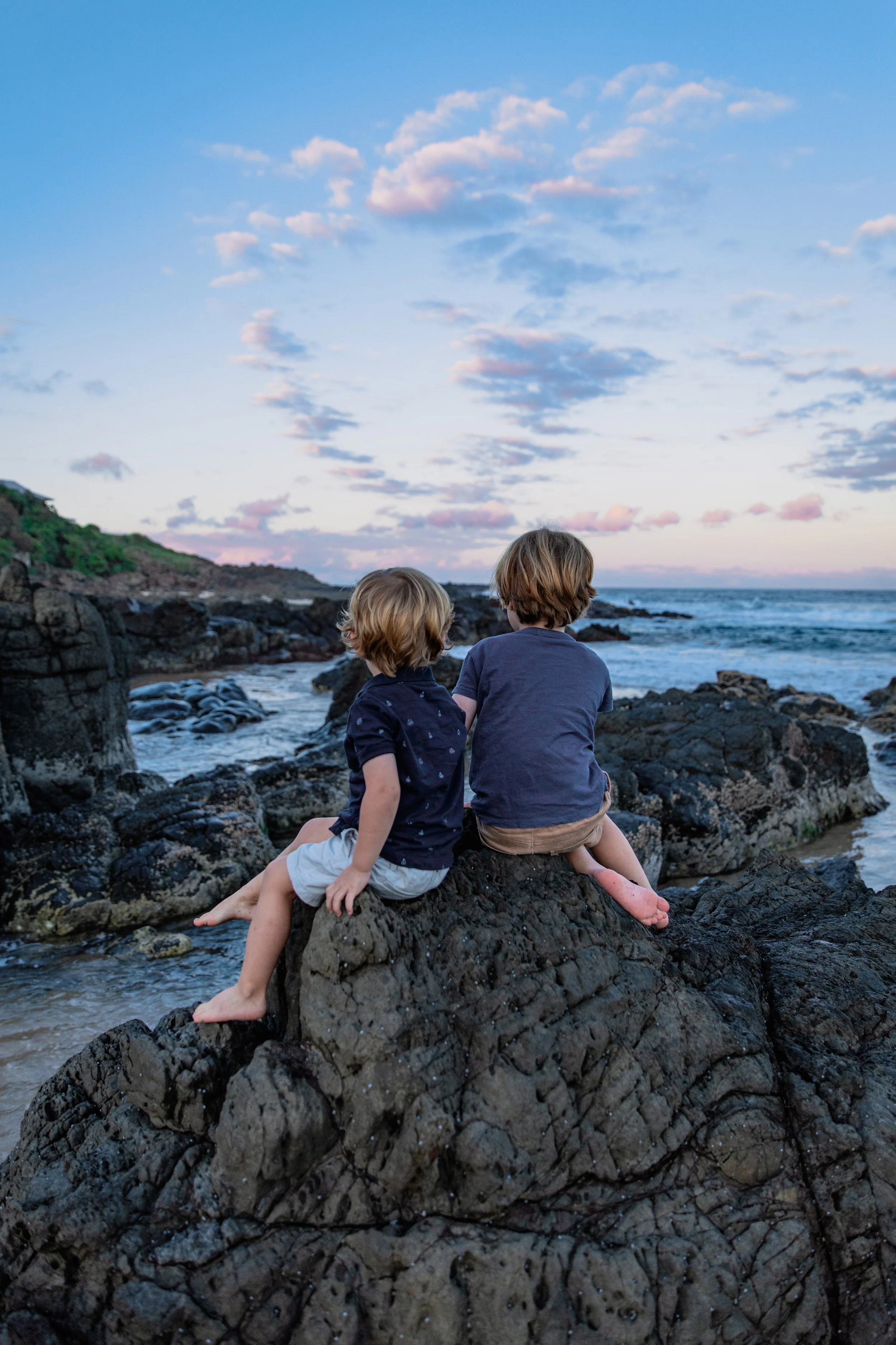 Two young children sitting on a rock looking out to sea