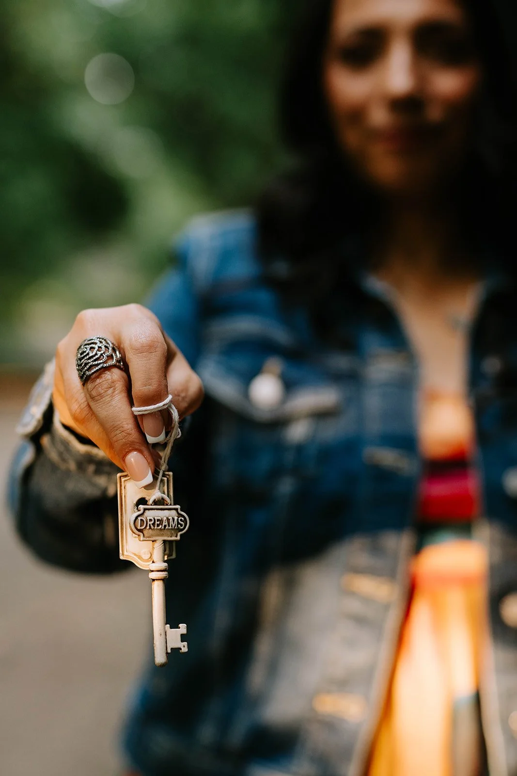 Cheryl Grant holding a key with a 'DREAMS' keychain in focus, blurred woman in denim jacket in background.