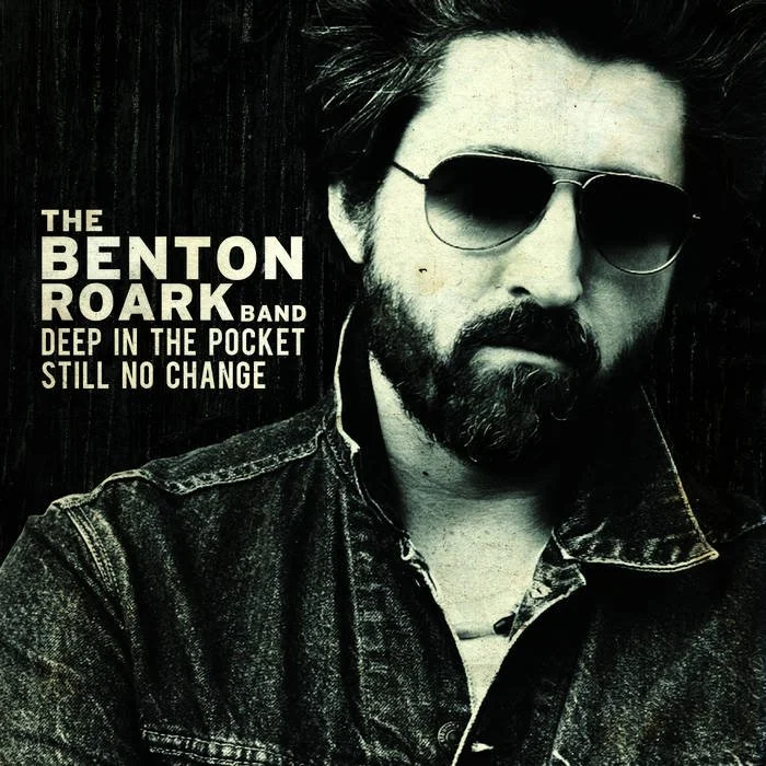 Black and white cover photo of a man with sunglasses and a beard, wearing a denim jacket, promoting The Benton Roark Band and their album 'Deep in the Pocket Still No Change'.