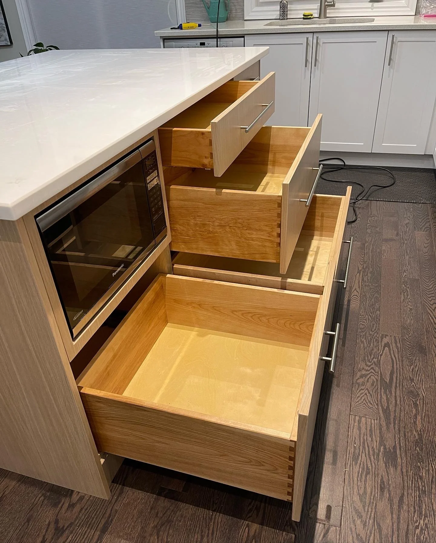 Custom crafted kitchen drawers inside a wood cabinet with a countertop and white cabinets in the background.