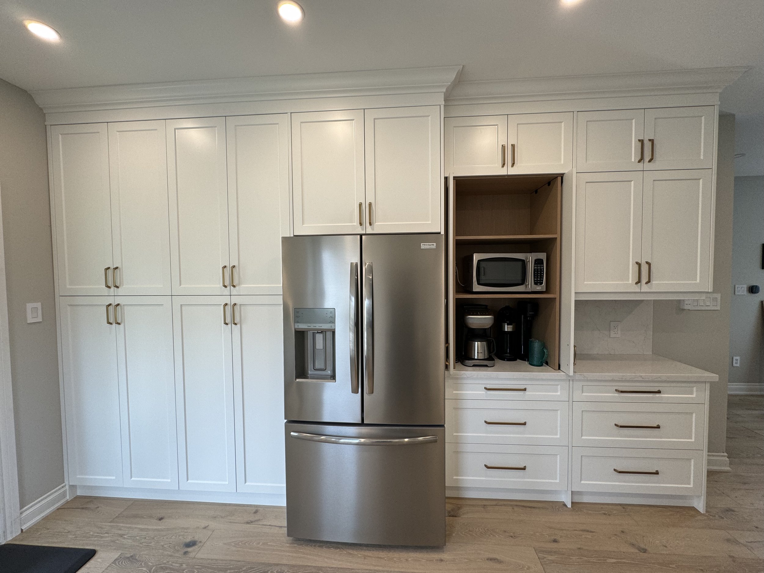 Modern Simcoe County kitchen with white cabinets, stainless steel refrigerator, and small appliances on open shelves.