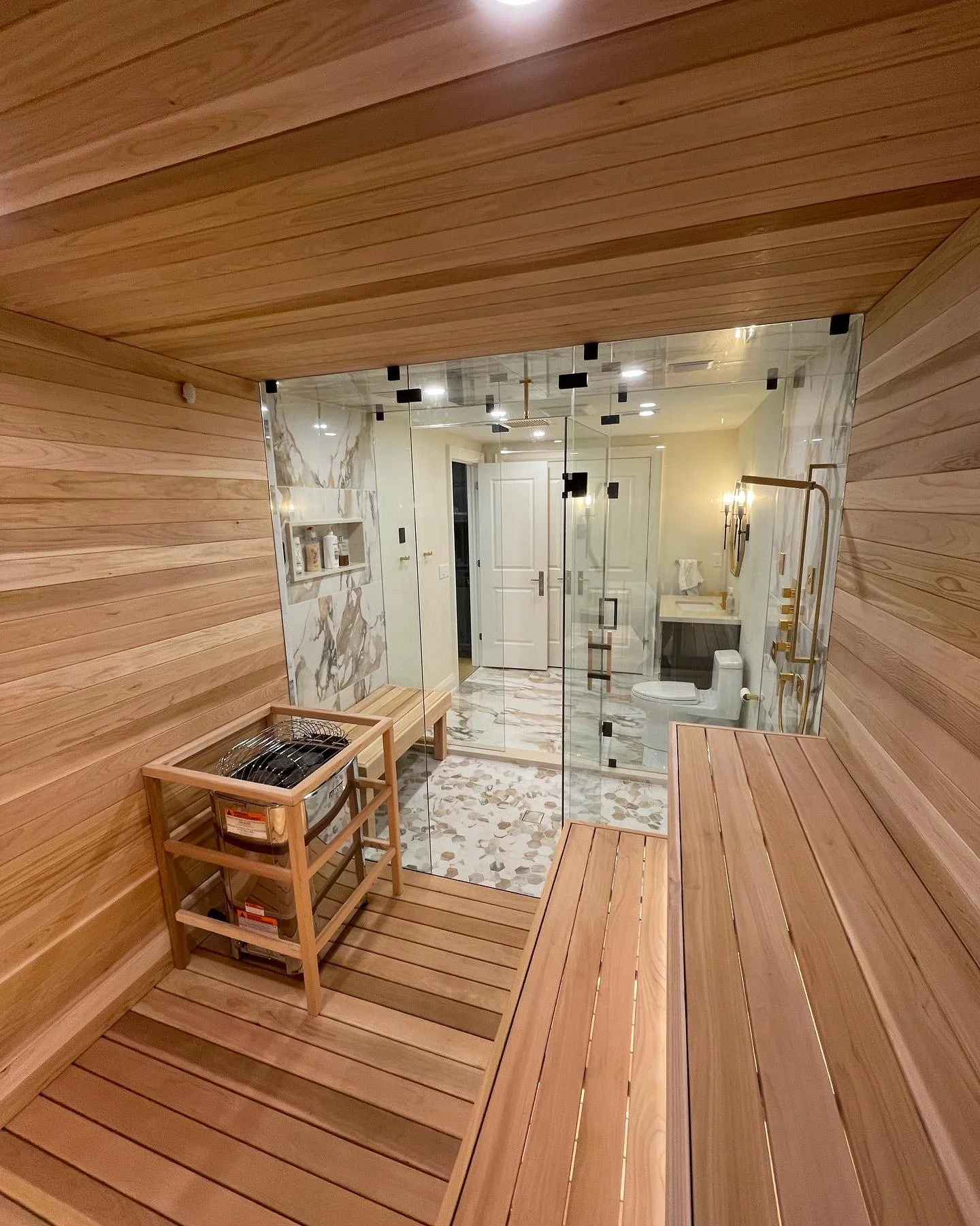 A luxurious bathroom with wood-paneled walls and benches, a glass-enclosed shower with marble tiles, and a separate toilet area.