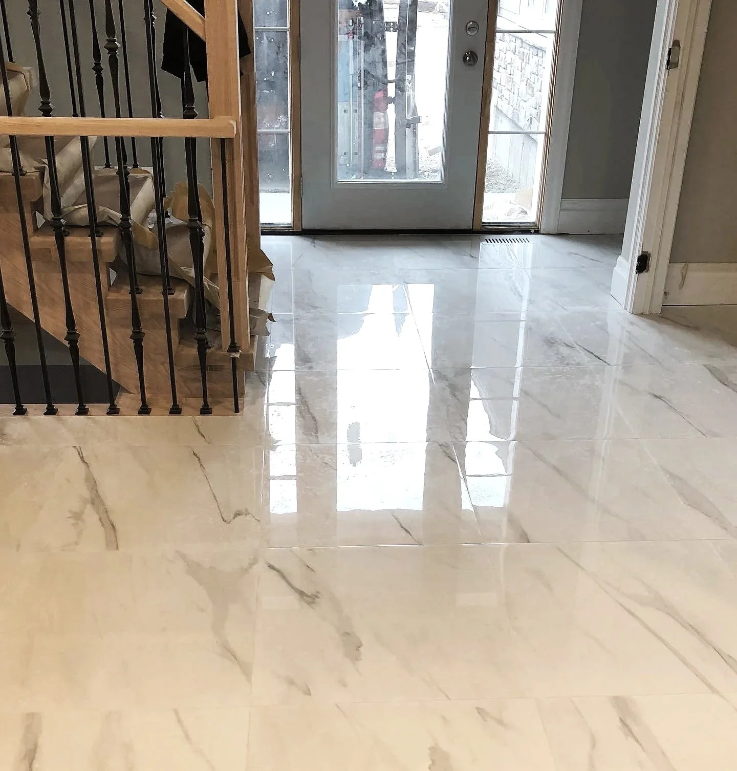 Interior view of a shiny white marble floor near a glass-paneled door, with staircase on the left side.