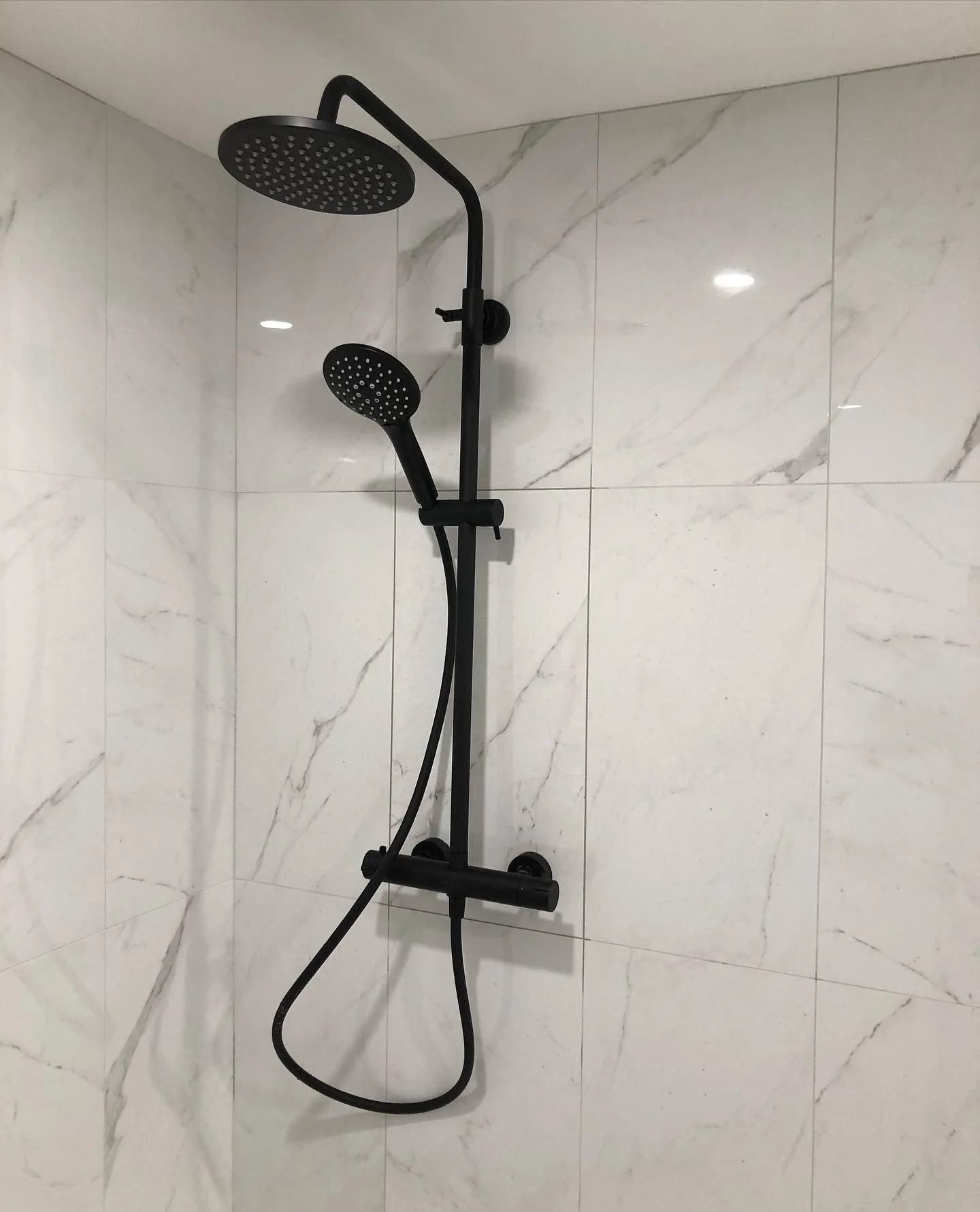 Black shower panel with two round shower heads installed on a tiled bathroom wall in Tiny Beaches, Ontario.