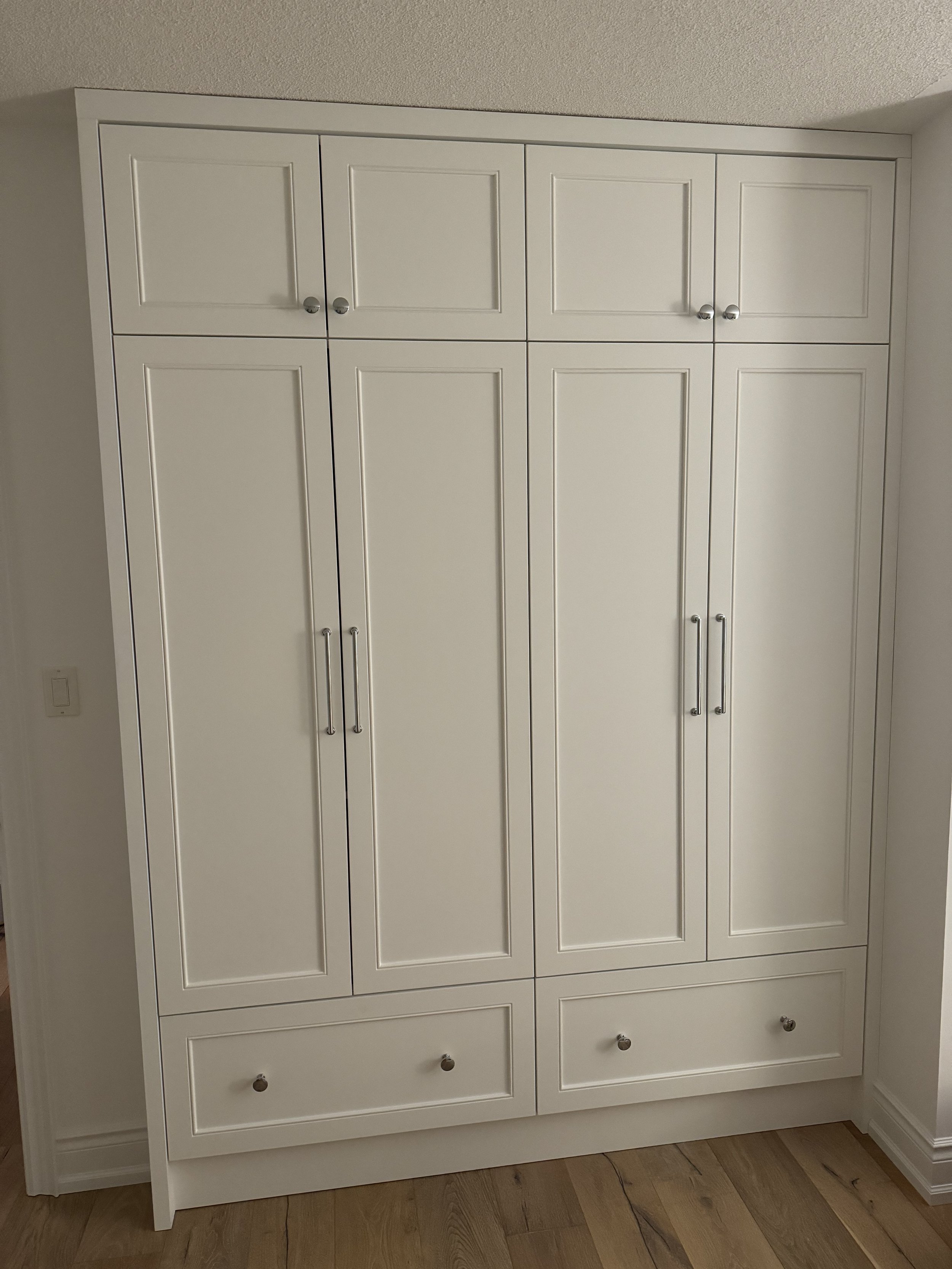 White custom built-in wardrobe in Simcoe County with multiple doors and drawers in a room with wooden floor.