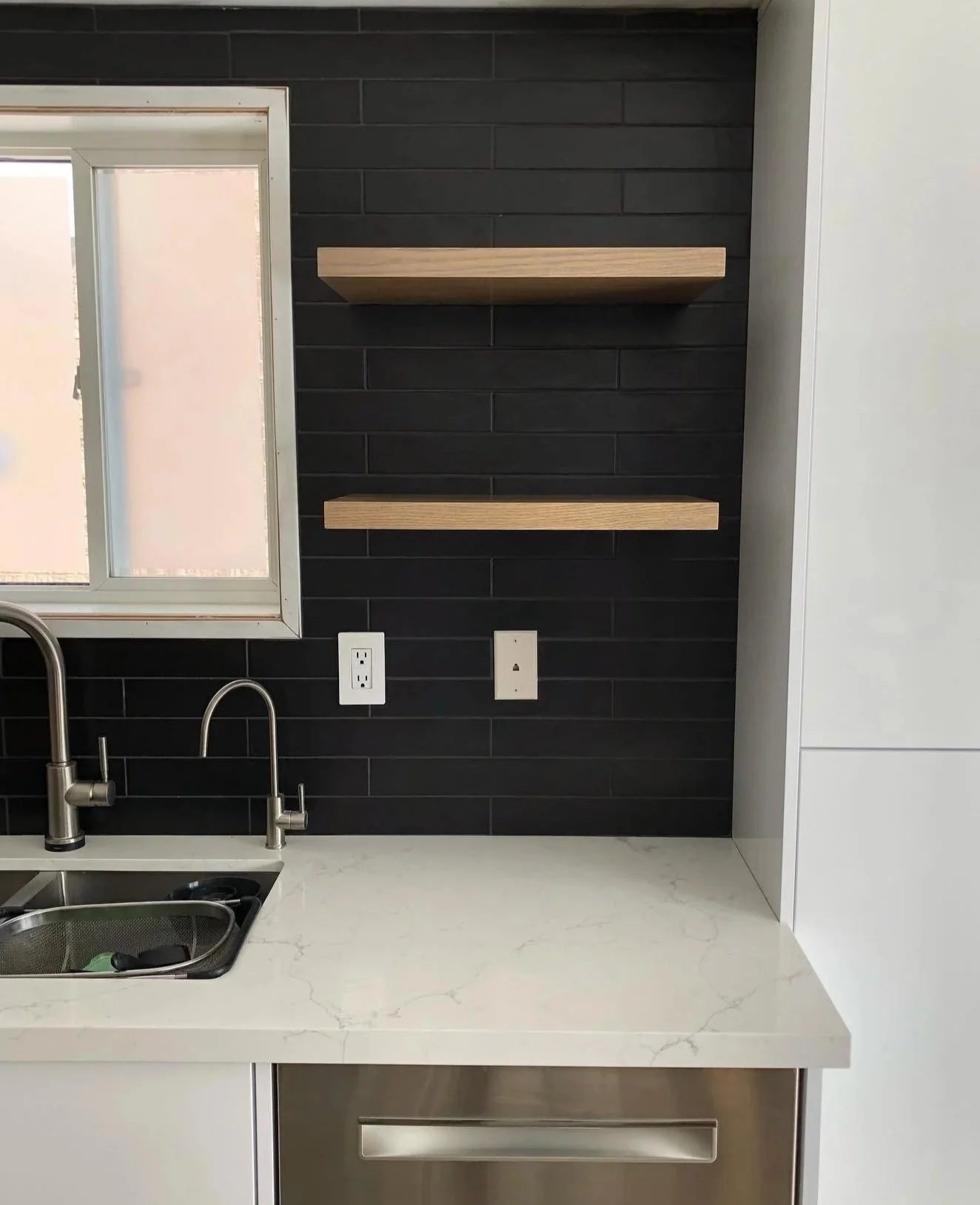 South Georgian Bay kitchen with black tiled wall, white countertop, stainless steel sink, window, and two wooden shelves.