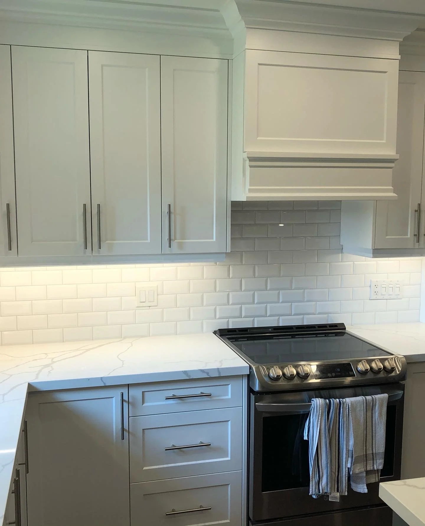 Modern kitchen with white cabinets, marble countertop, subway tile backsplash, and stainless steel stove with striped towels hanging on the oven handle.