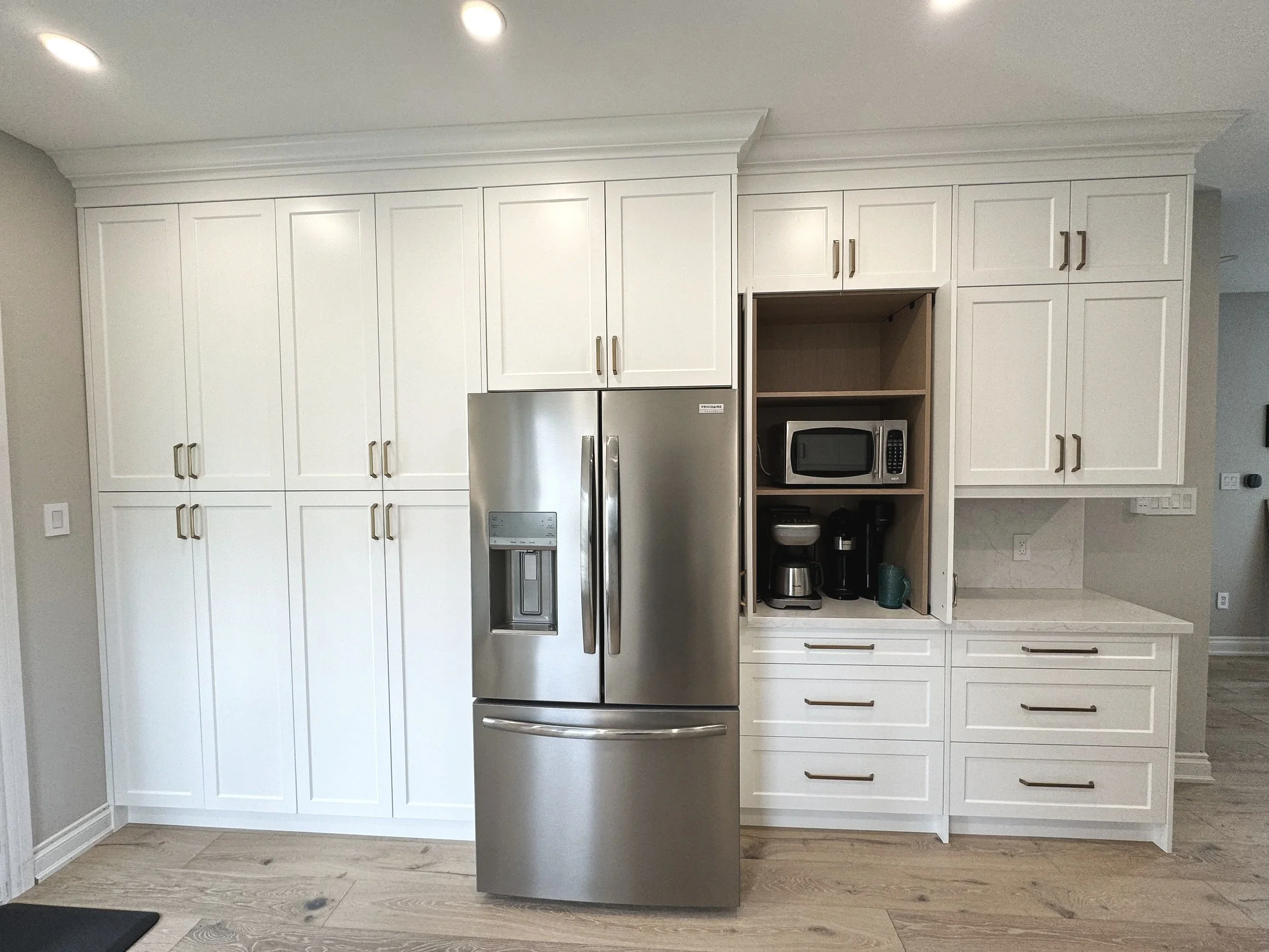 Modern Collingwood kitchen with white cabinets, stainless steel refrigerator, and a built-in shelf holding microwave, coffee maker, and kettle.