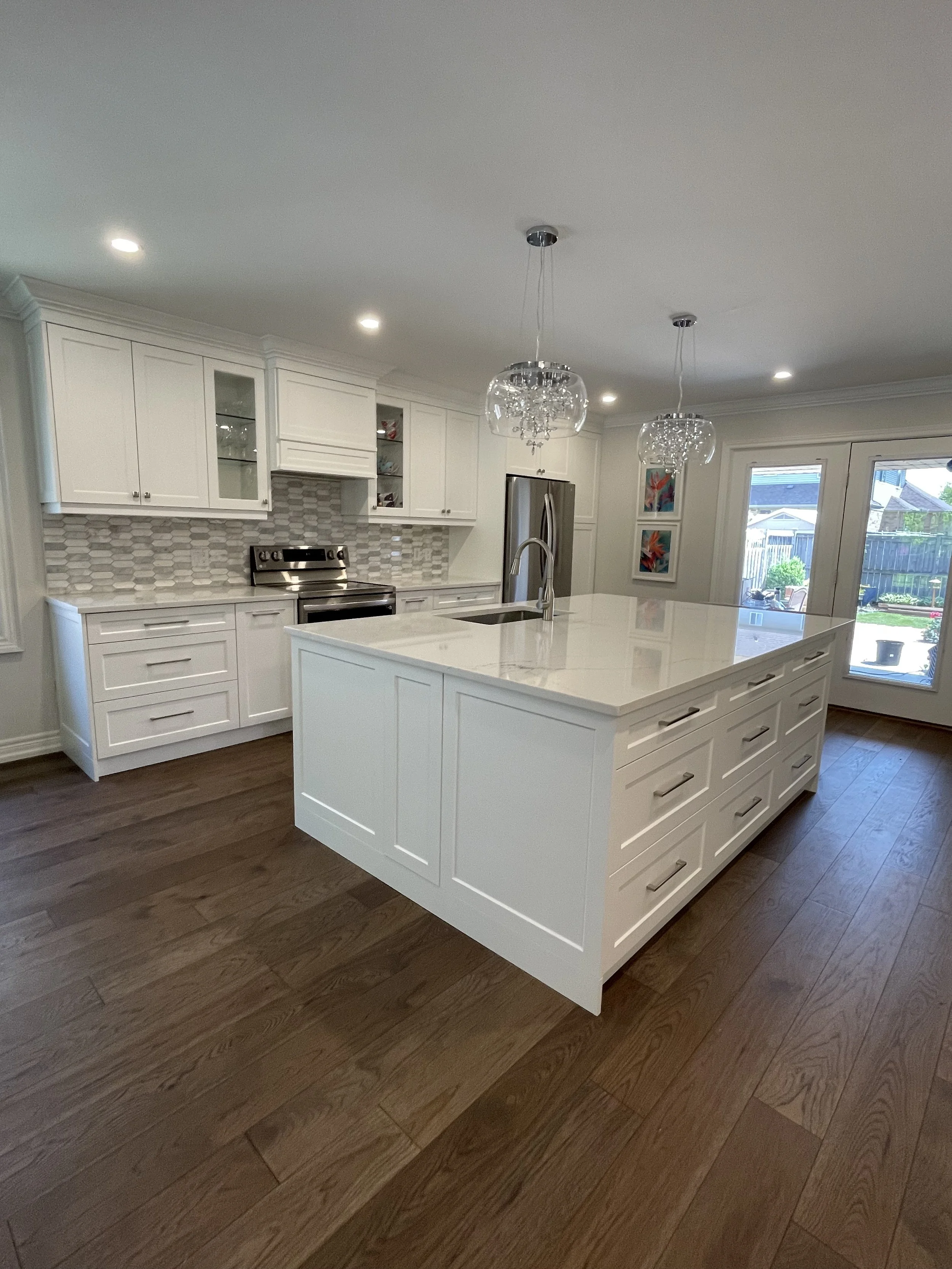 Modern kitchen with white cabinets, a large island, stainless steel appliances, pendant lights, and hardwood flooring.