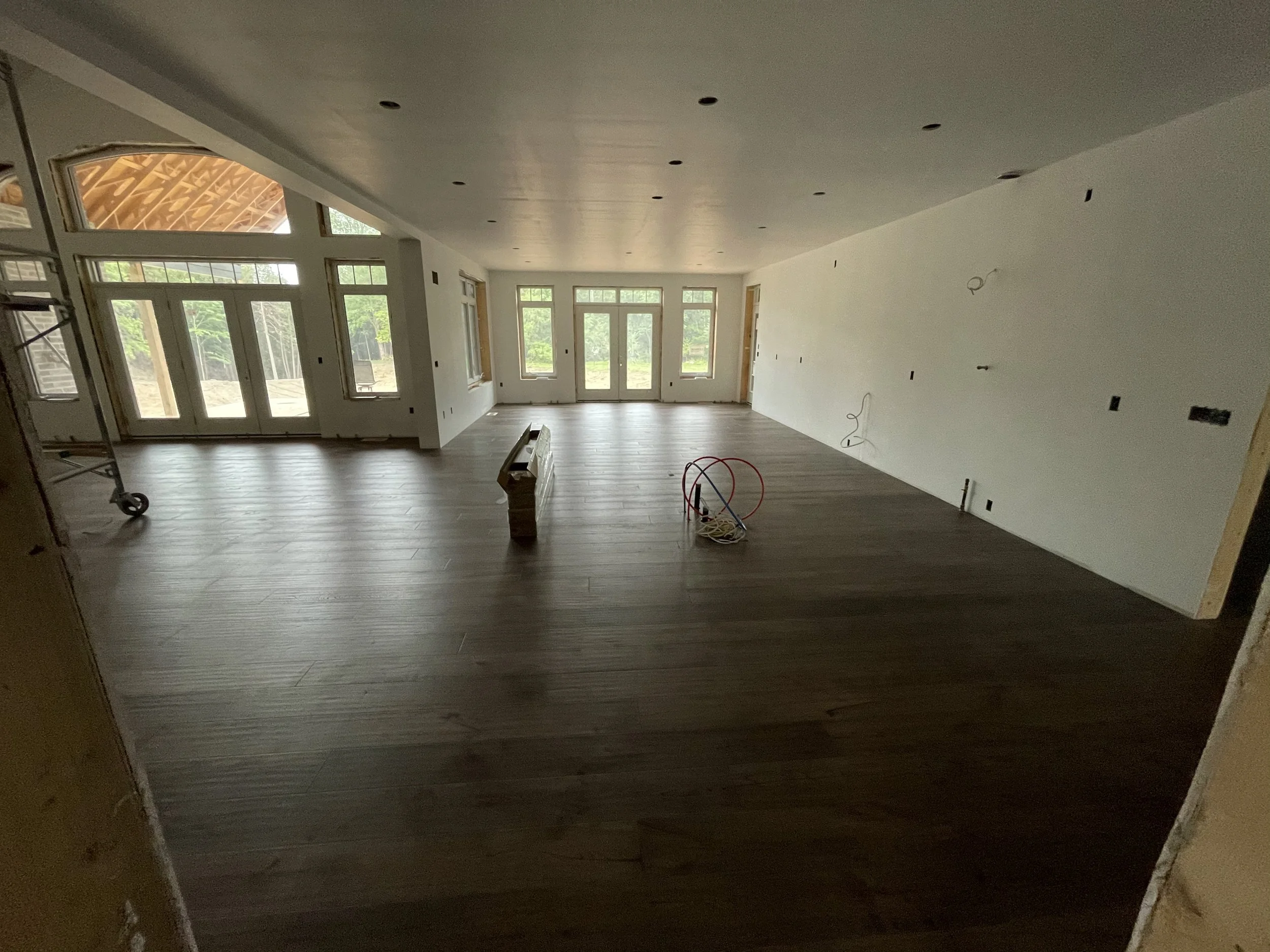 Interior of a house renovation with wood flooring, multiple windows, and electrical wiring visible.