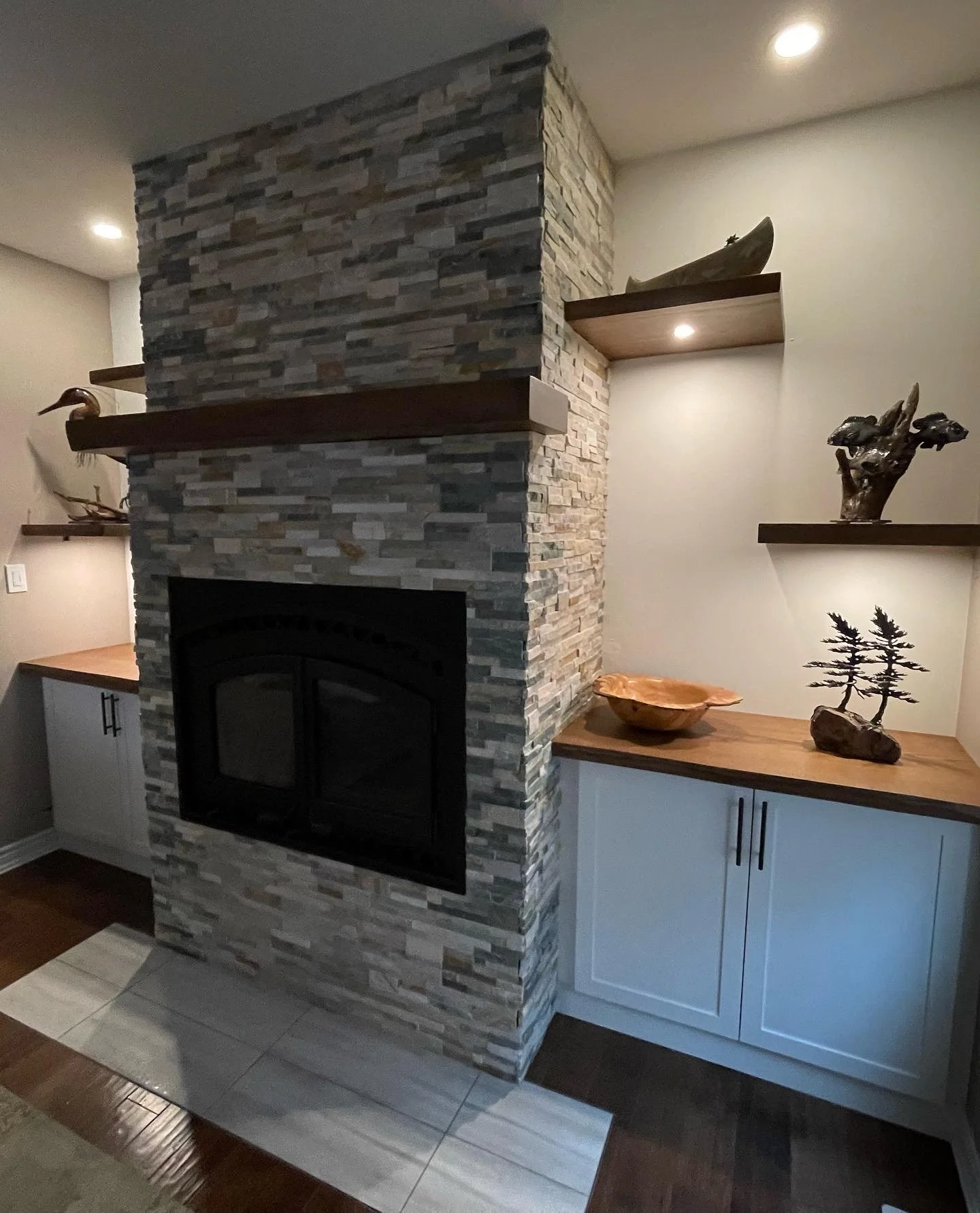 Living room with a stone fireplace, built-in shelves with decorative items, and a wooden countertop with cabinets.