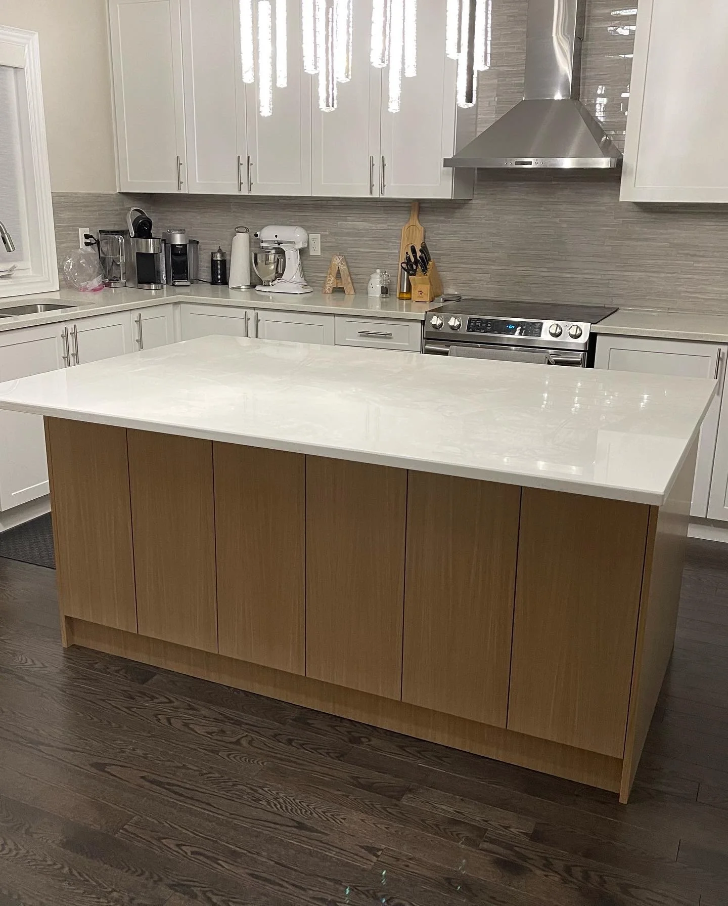 Modern kitchen with a white countertop island, white cabinets, stainless steel appliances, including a stove and range hood, and various small appliances and utensils on the back counter.