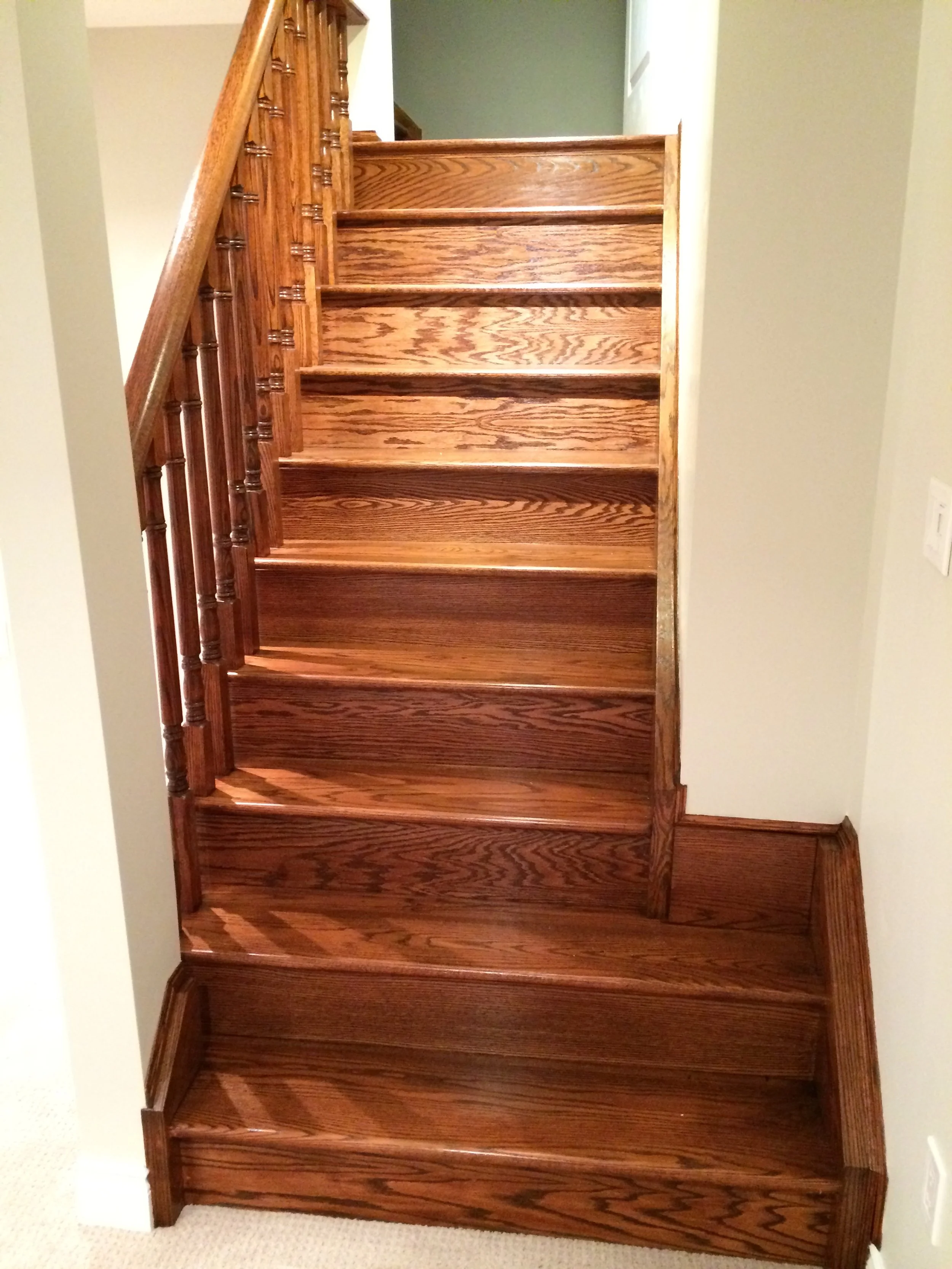 Wooden staircase with multiple steps, a carved baluster handrail, and a beige carpeted floor at the bottom.