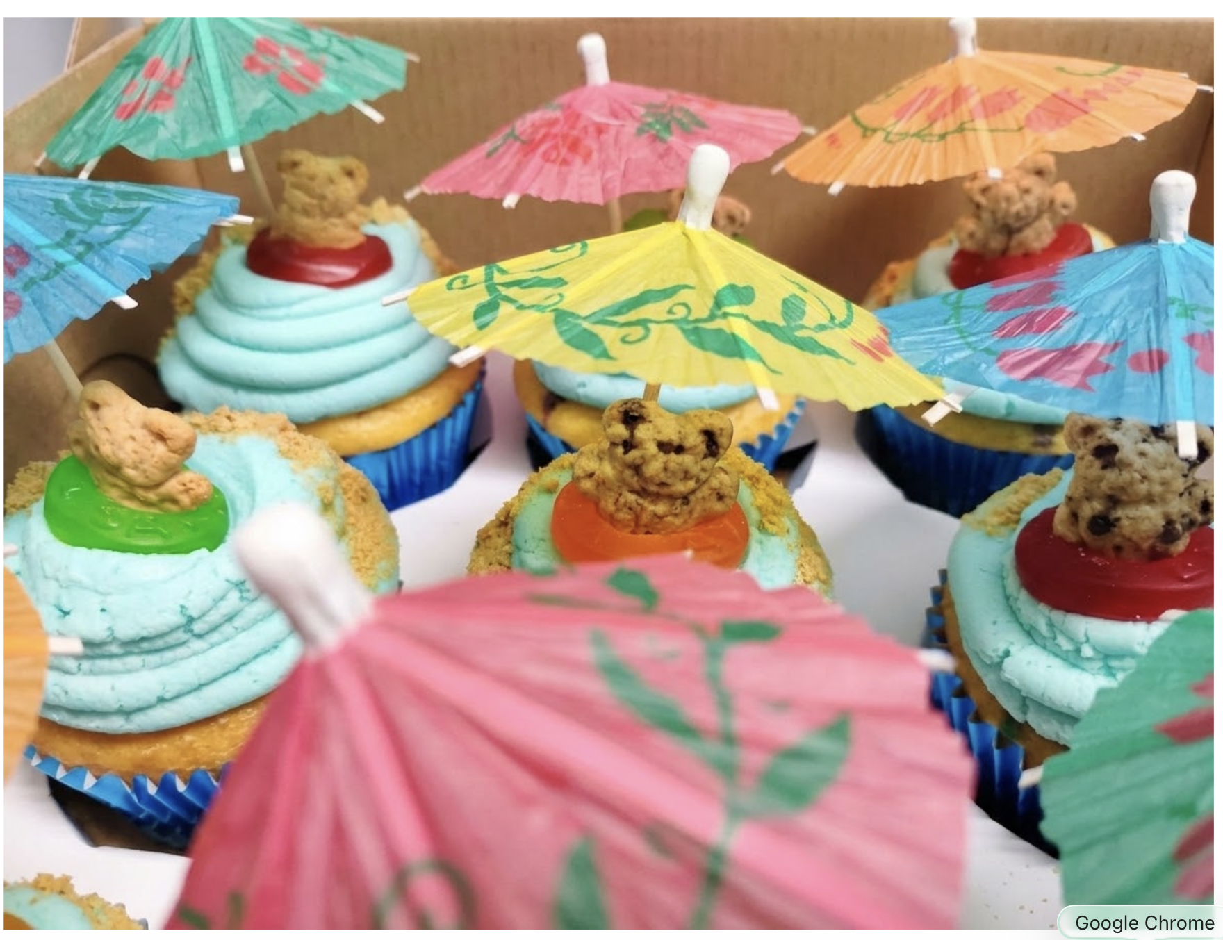 Cupcakes decorated with colorful umbrellas and teddy bear toppers.