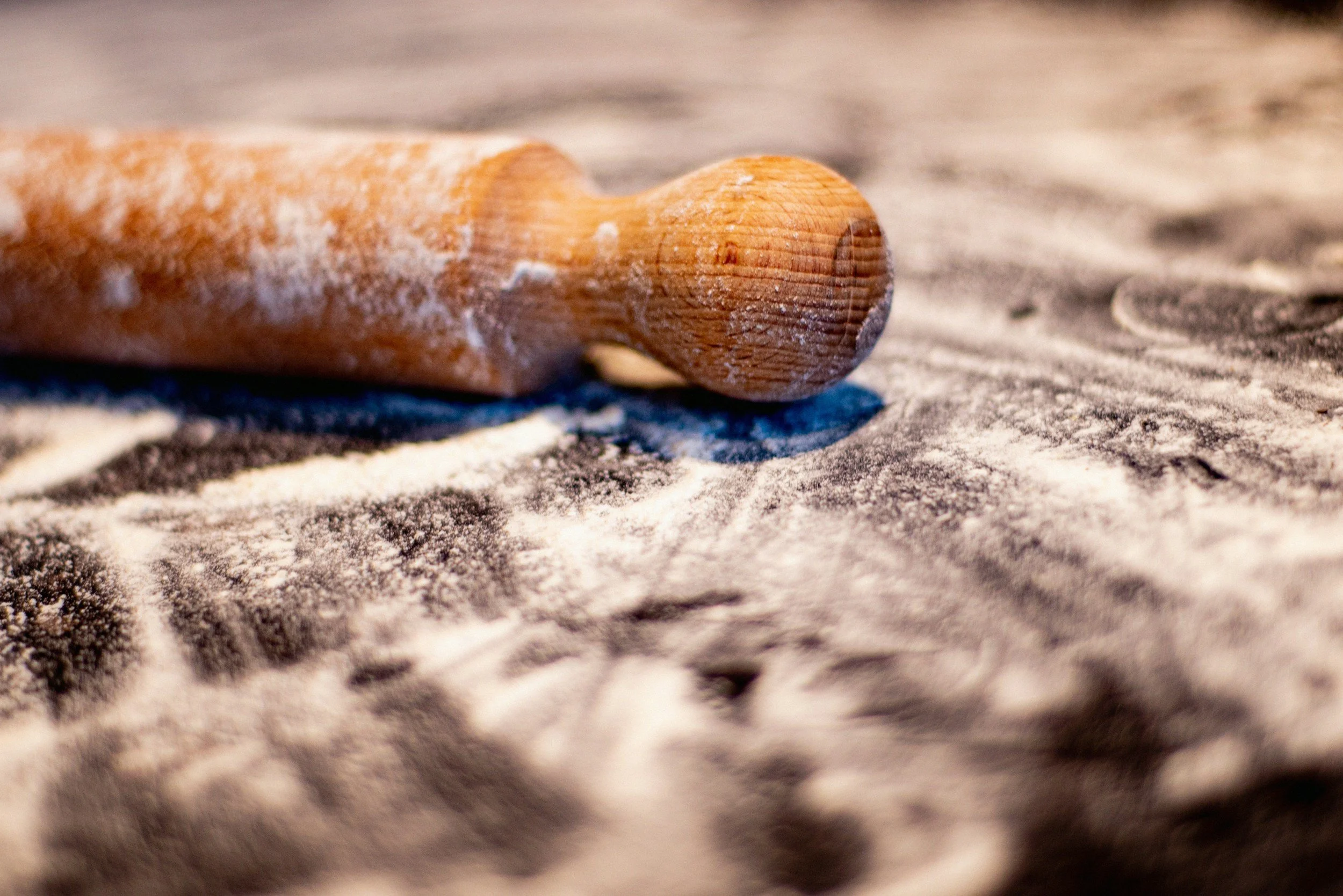 A wooden rolling pin resting on a surface dusted with flour.