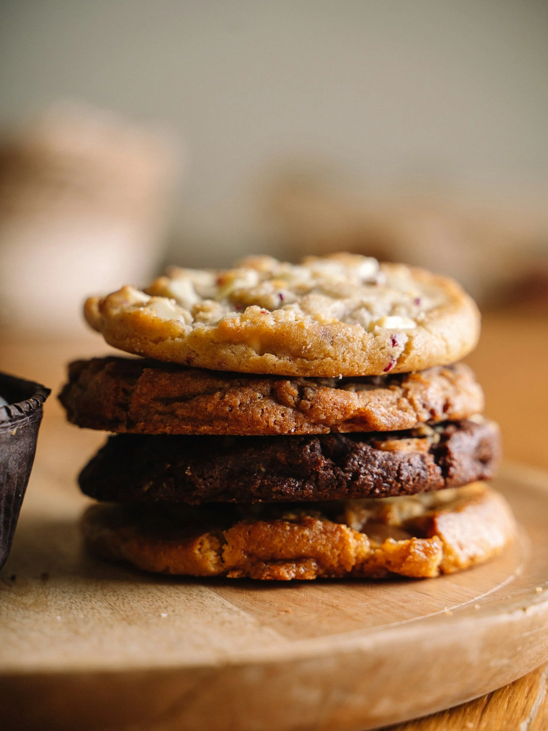 A stack of assorted cookies on a wooden surface, with various textures and chocolate chips.