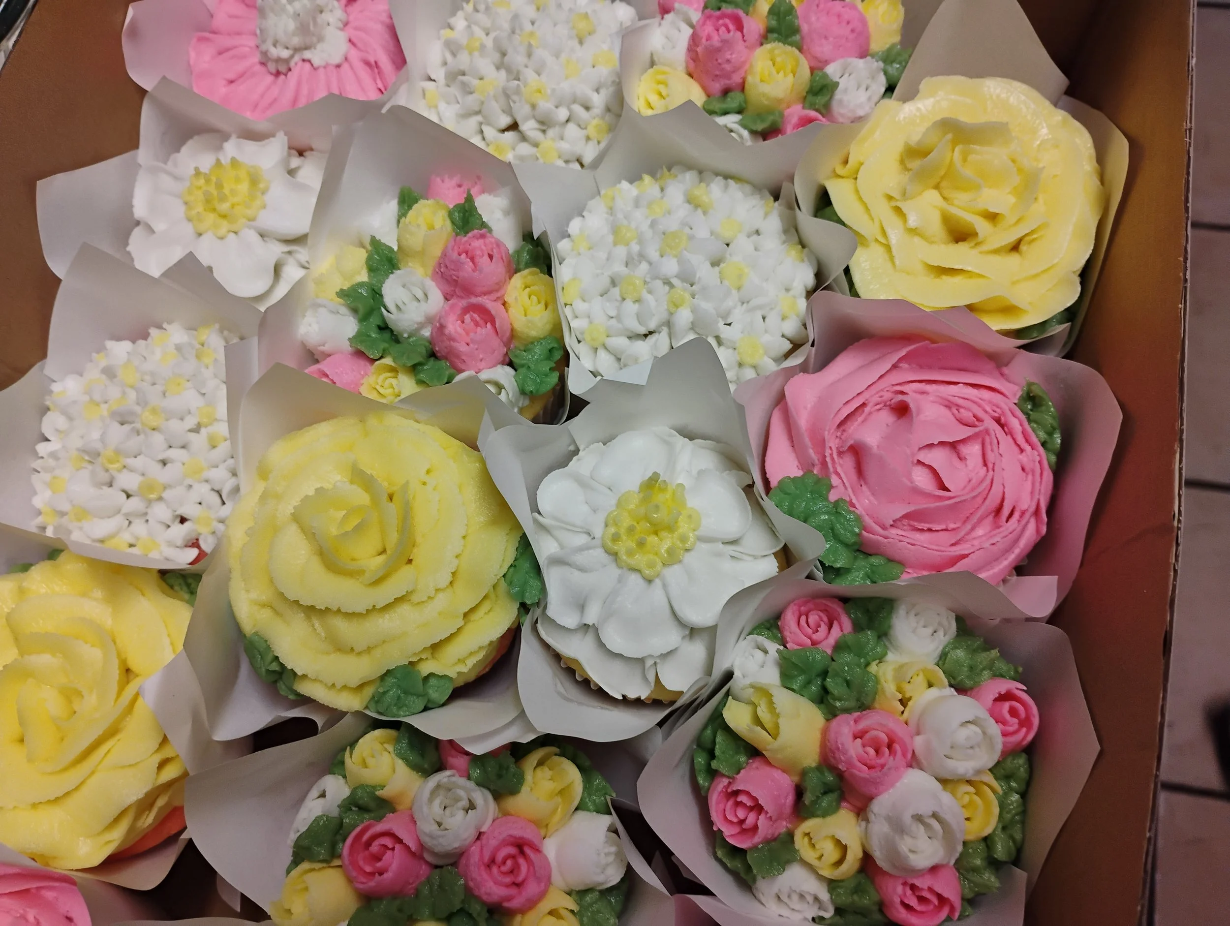 Box of turquoise cupcakes with frosting arranged in a grid pattern, wrapped with a dark blue satin ribbon tied in a bow.