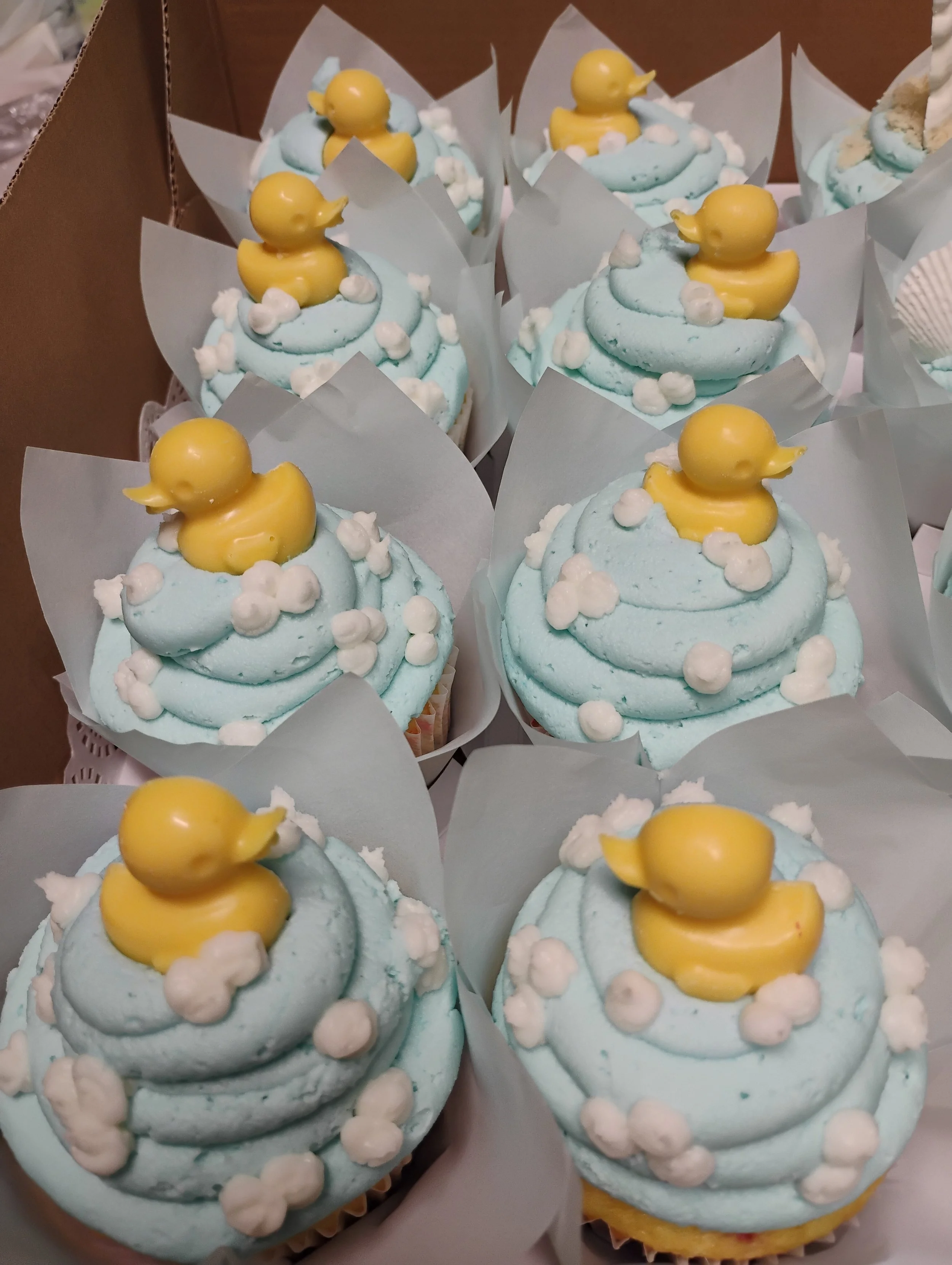 Cream cupcakes decorated with yellow rubber duck toppers and white edible pearls, wrapped in white cupcake liners.