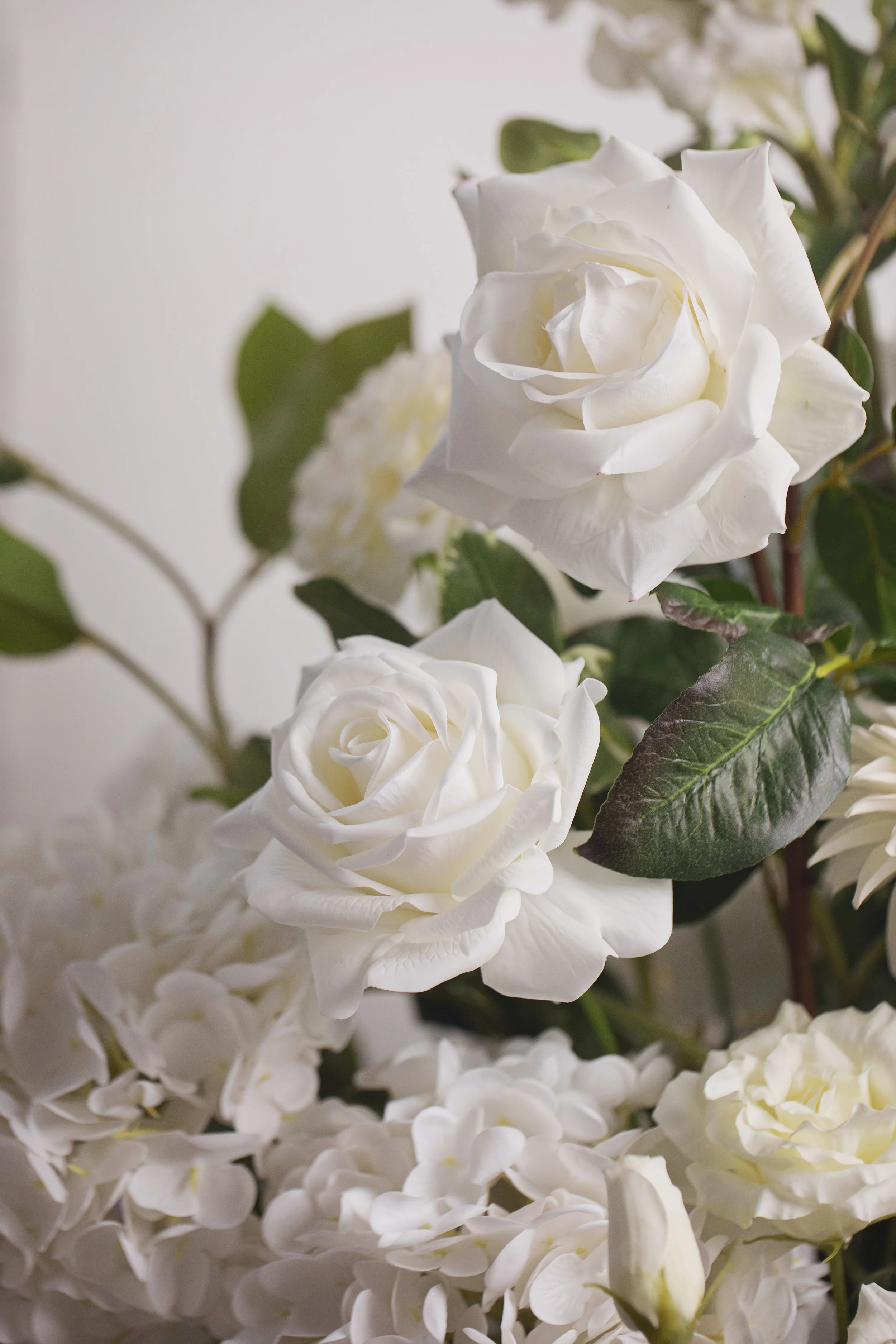 Close-up of white roses and hydrangeas with green leaves, arranged in a floral display.