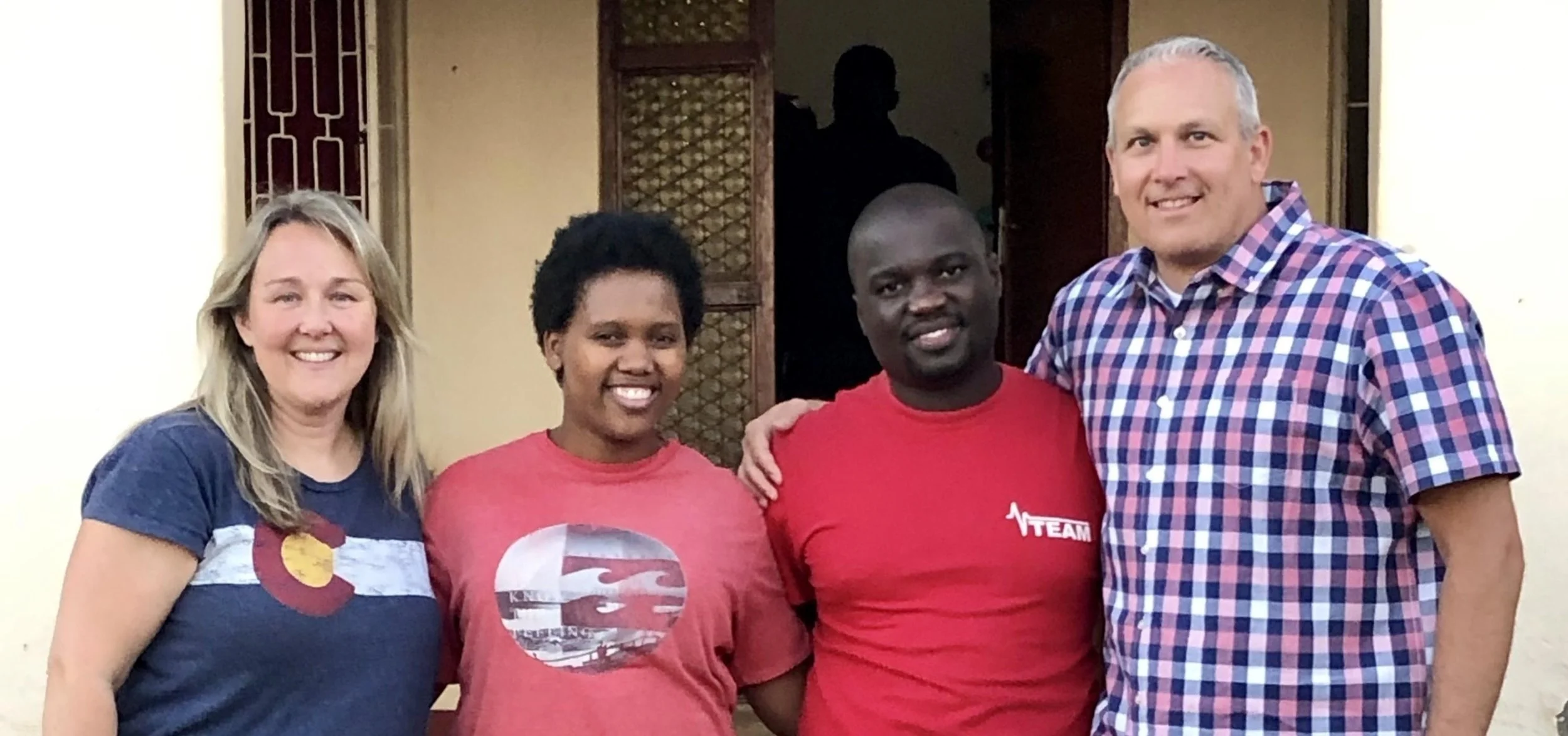 Four people standing together, smiling for the camera in front of a doorway.