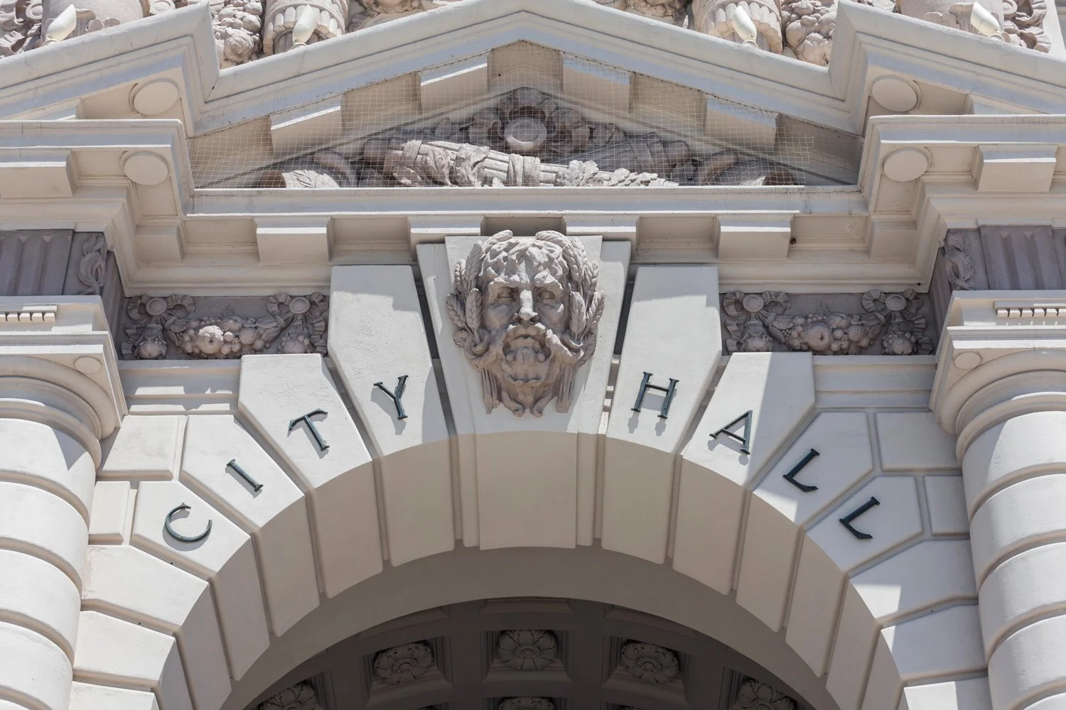 Close-up of the building entrance with the words 'CITY HALL' and a carved face with a beard and mustache above the archway.