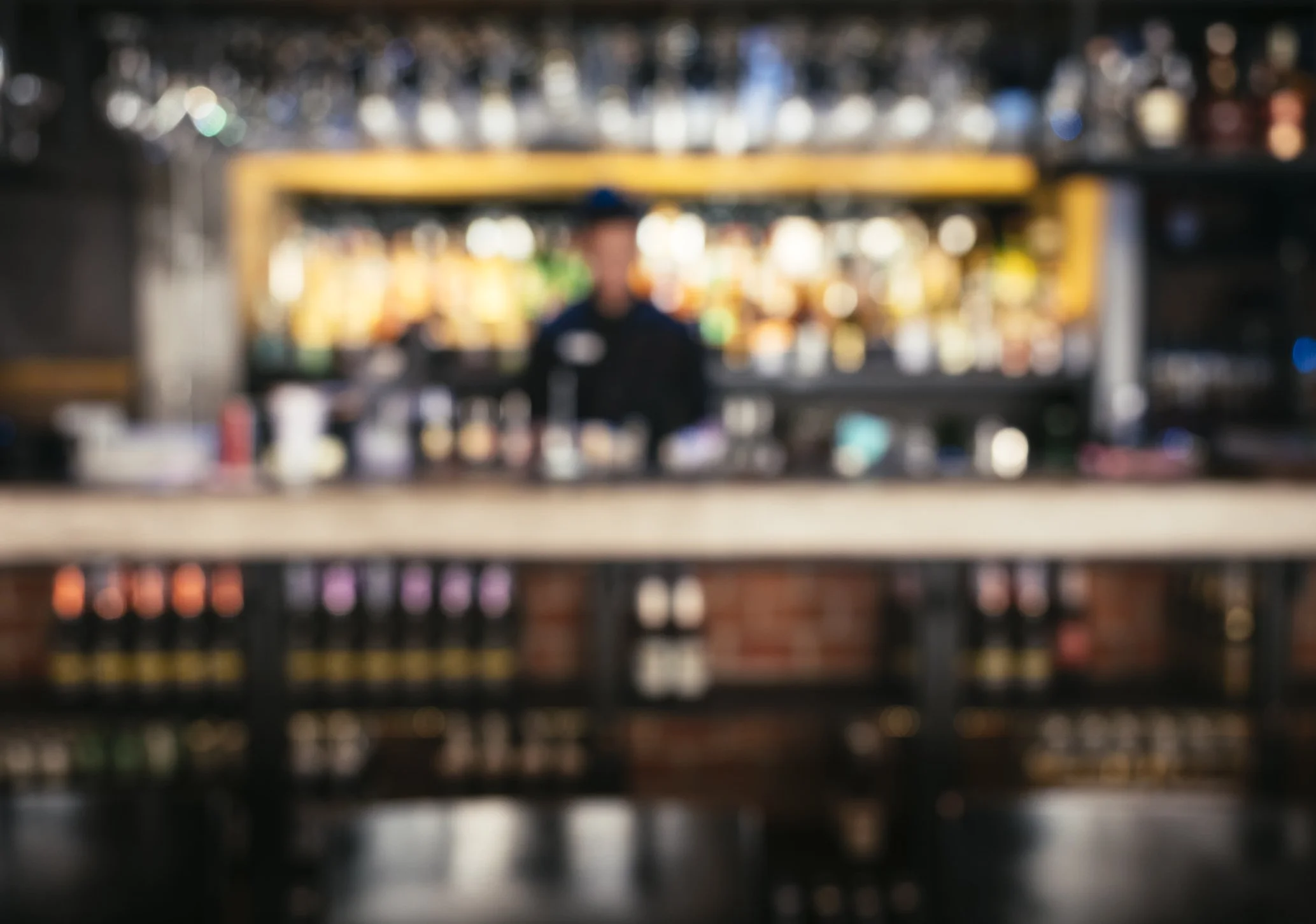 Blurred image of a bartender behind a bar with colorful bottles in the background.