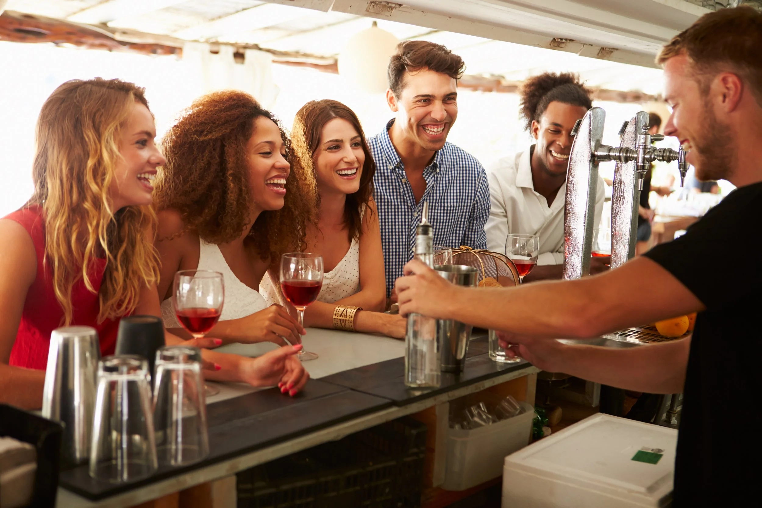 People having a great time at a bar as the bartender serves cocktails.