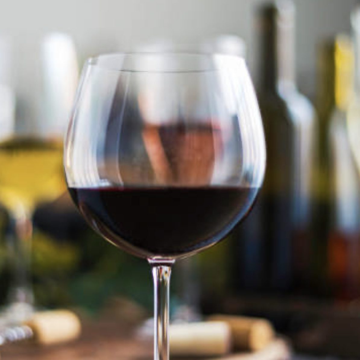 A glass of red wine with blurred bottles in the background.