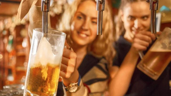 Two women at a bar pouring beer from taps, smiling and having a great time.