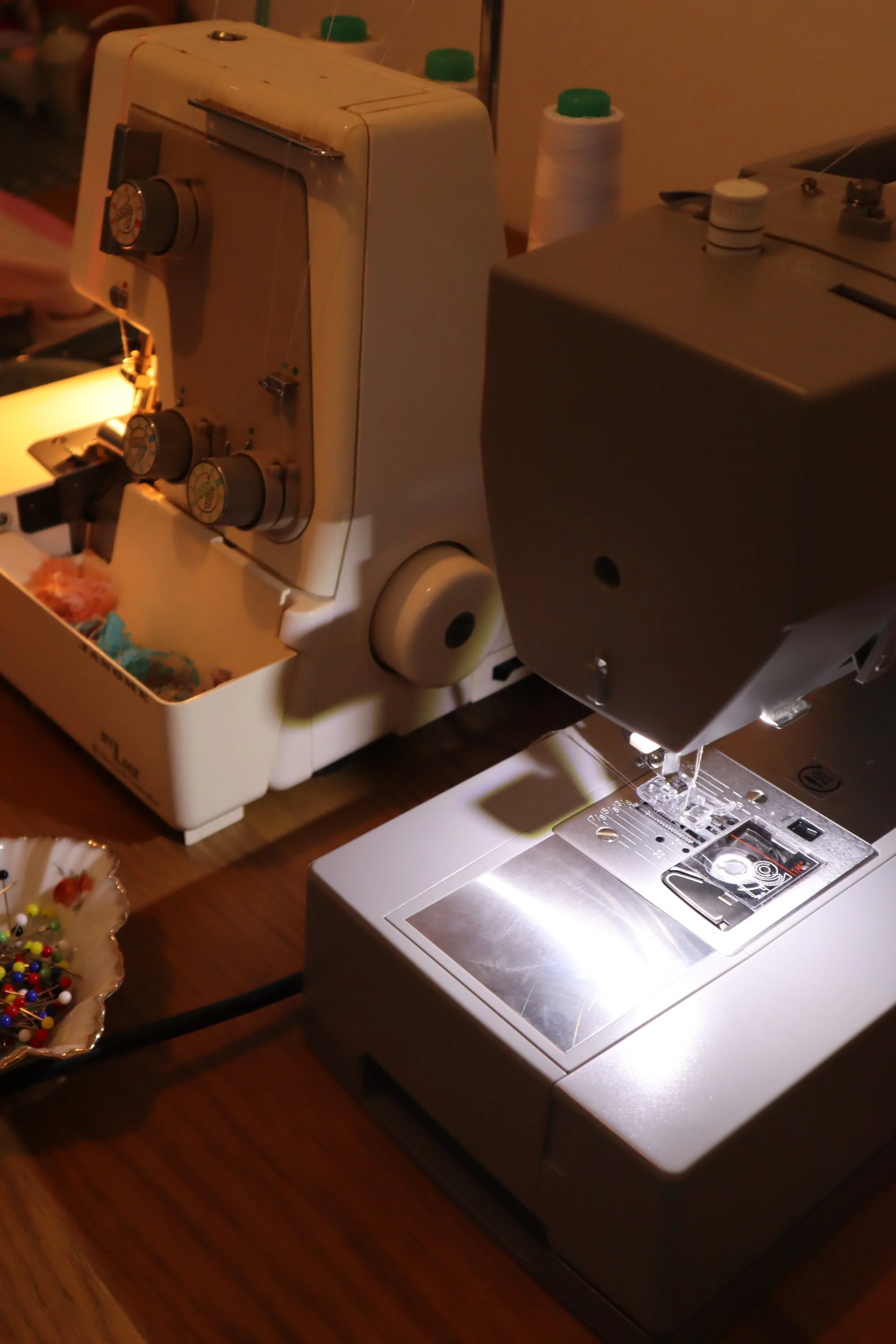 Close-up of a sewing machine on a wooden table, with a container of pins nearby.