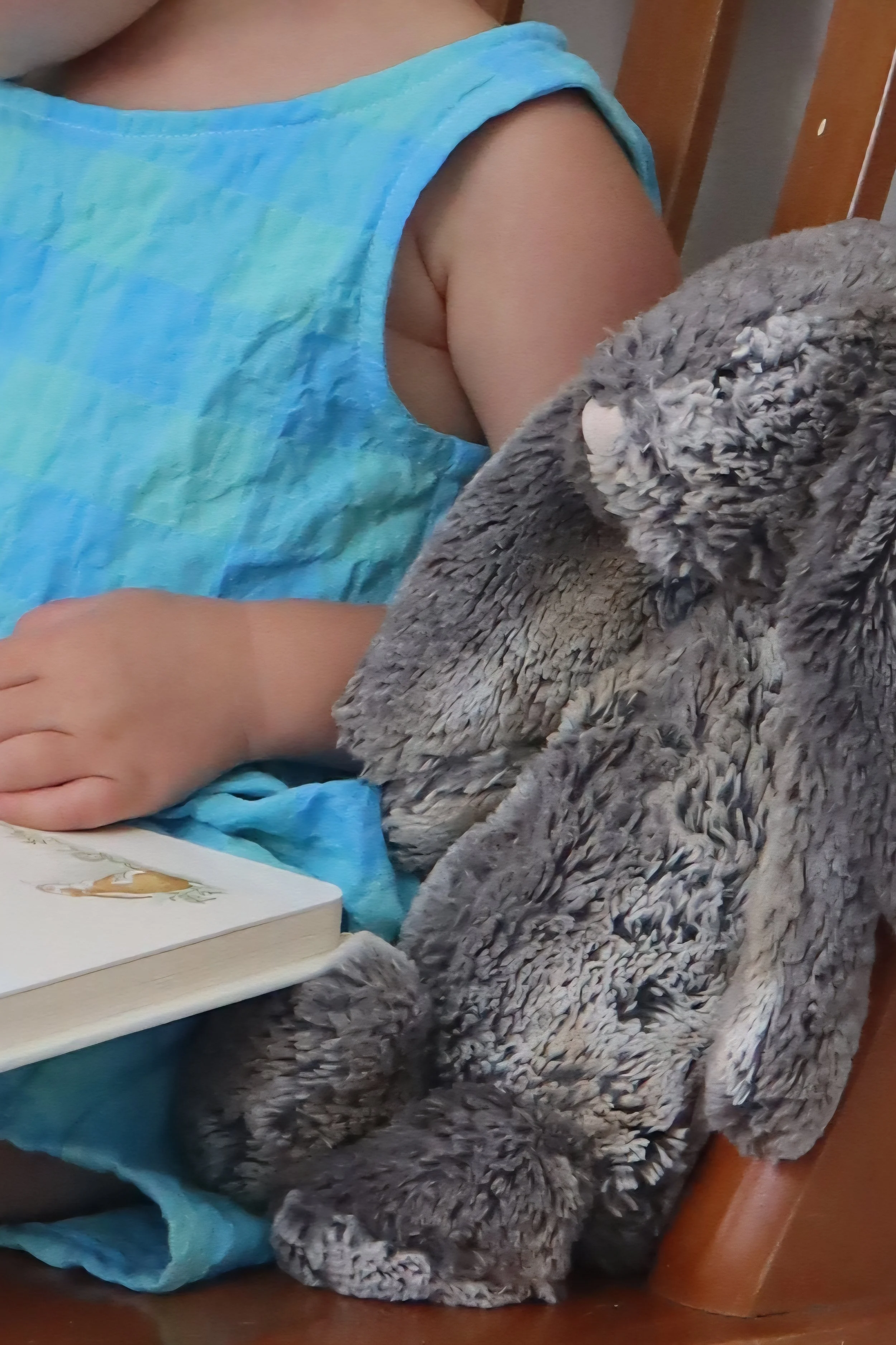 Child wearing a blue tie-dye shirt sitting at a table with a plush gray stuffed animal and a book.