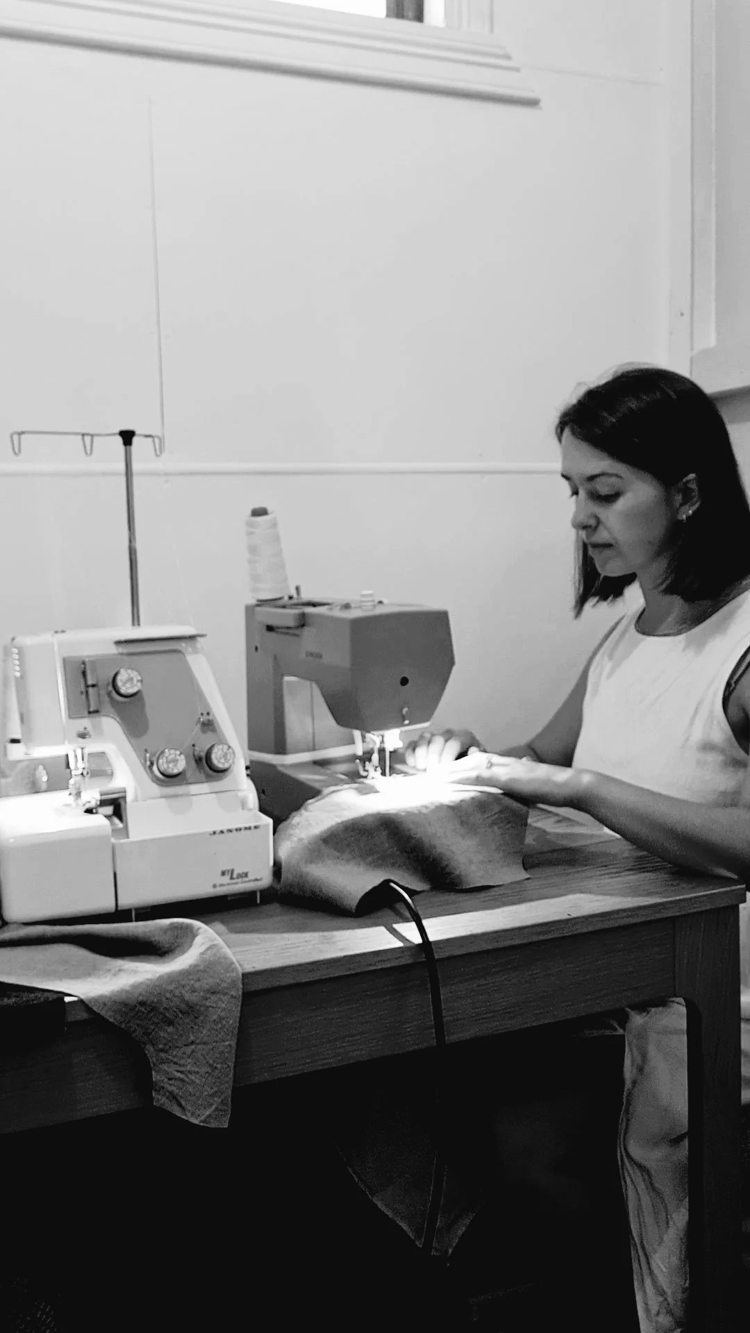 A woman sewing fabric on a sewing machine at a wooden table.