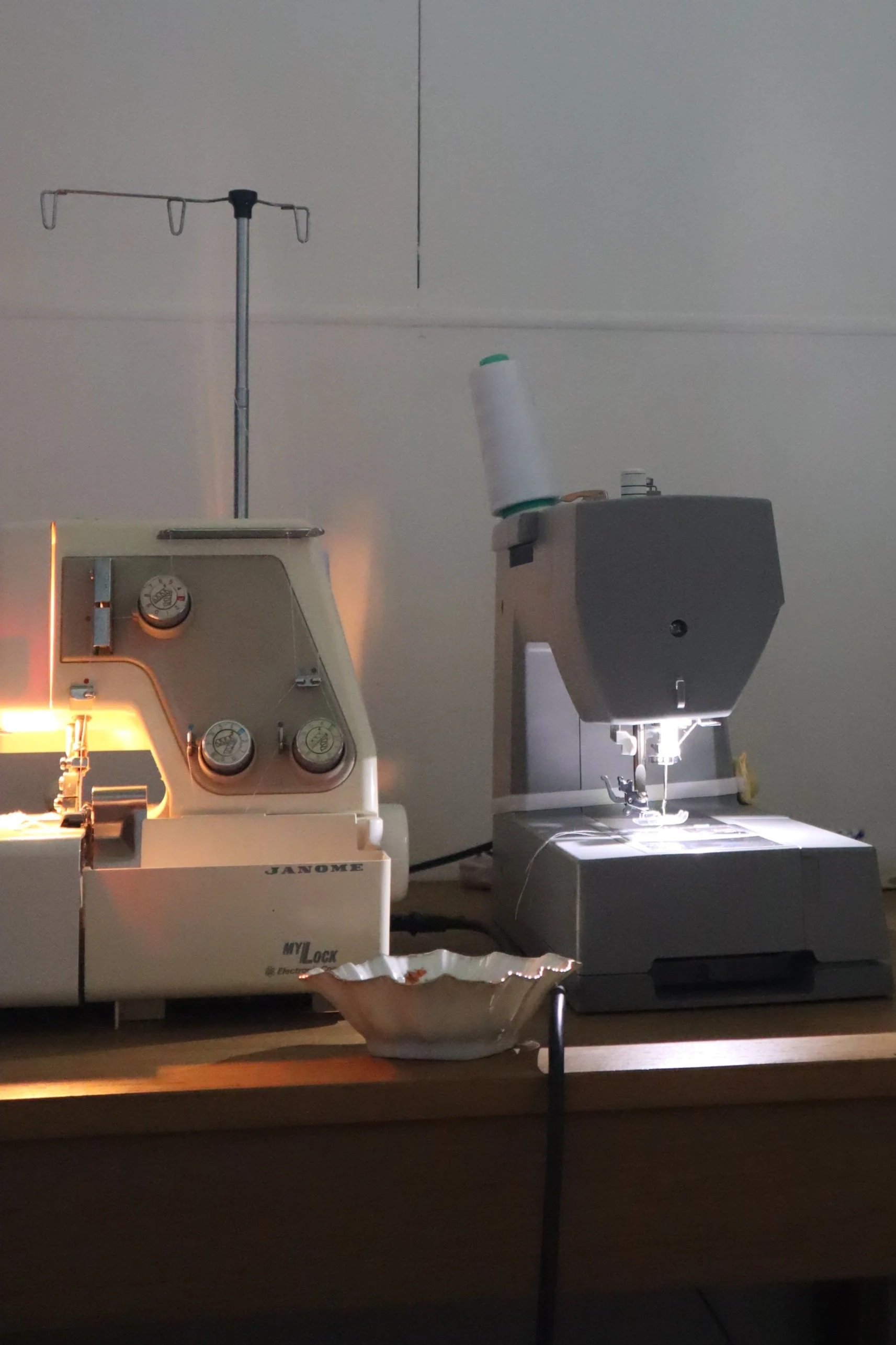 A sewing machine and embroidery machine on a wooden table with a bowl in front of them.