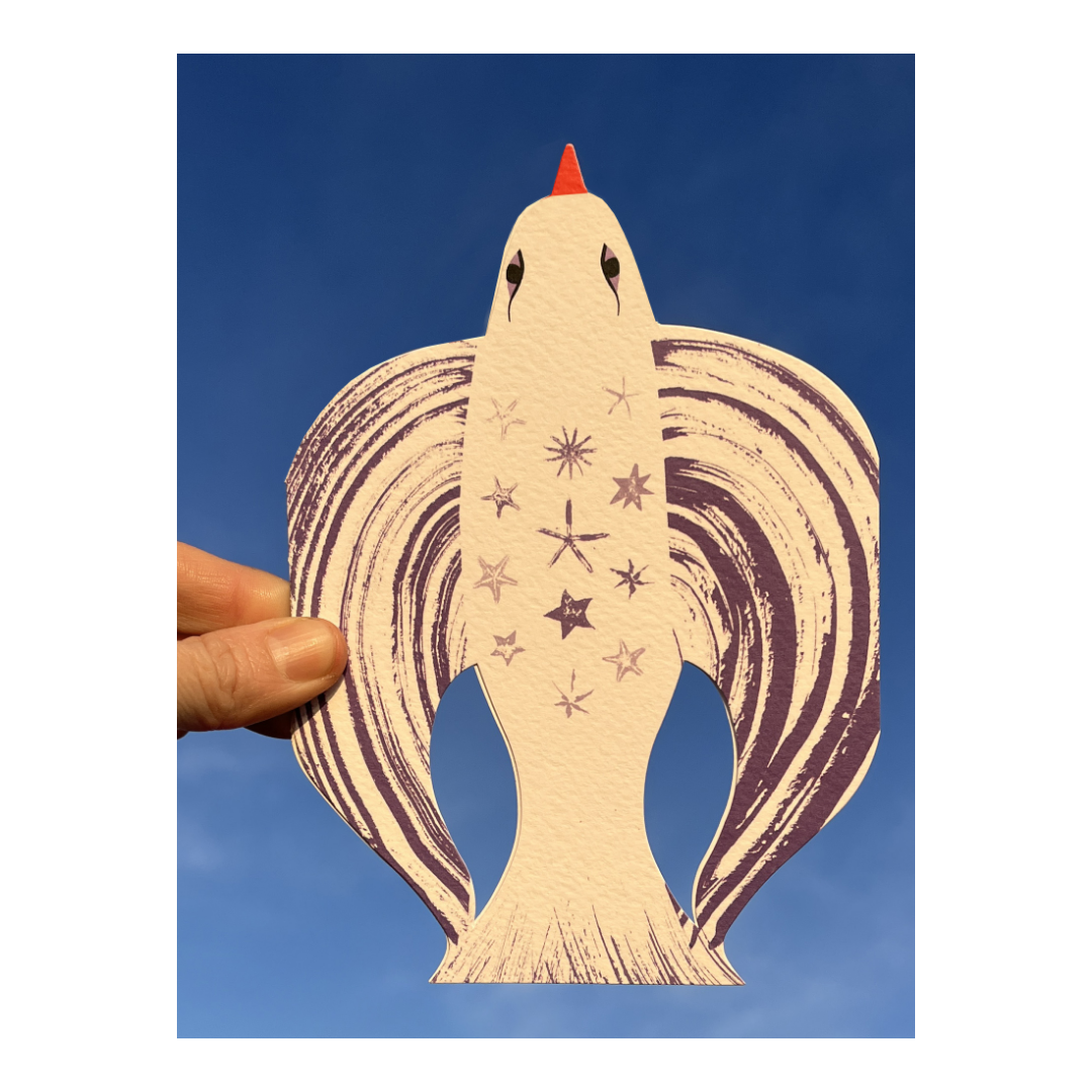 Hand holding up a star-shaped paper cutout of a seahorse with star and space motifs against a blue sky.