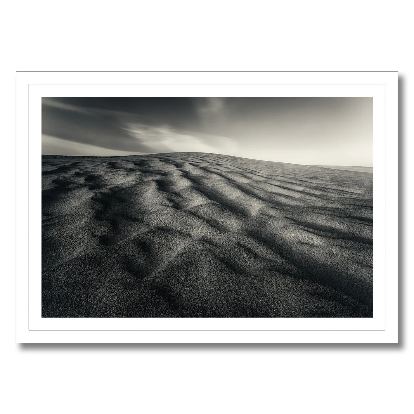 Black and white photograph of wind-sculpted sand dunes beneath a dramatic sky.